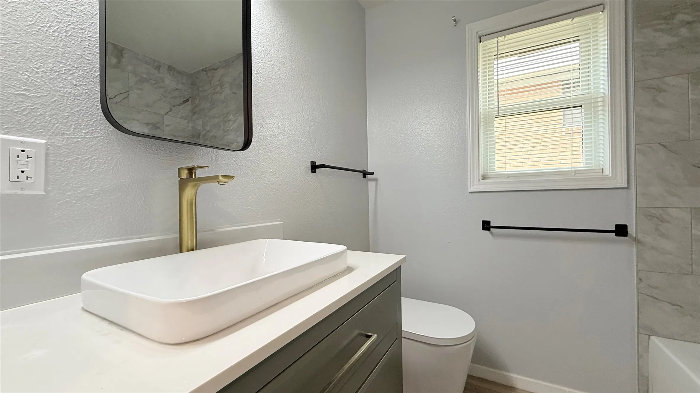 Bathroom vanity featuring a rectangular vessel sink, brushed brass faucet, matte black hardware, and light-toned countertop