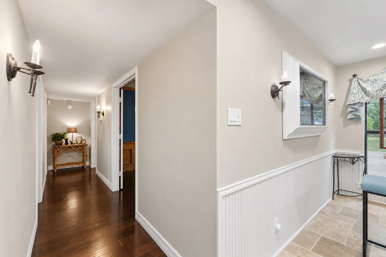 Interior corridor featuring wood-finish flooring, white beadboard wainscoting, and wall-mounted candle-style sconces