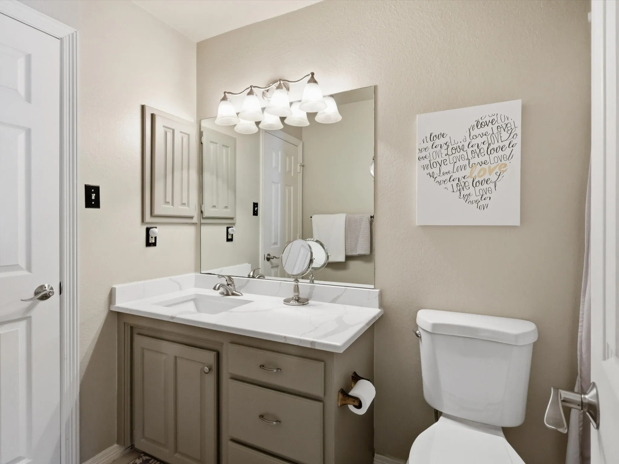 Bathroom vanity featuring a stone-composite countertop with integrated sink, undermount faucet, multi-drawer cabinetry, and a wall-mounted light fixture above a framed mirror