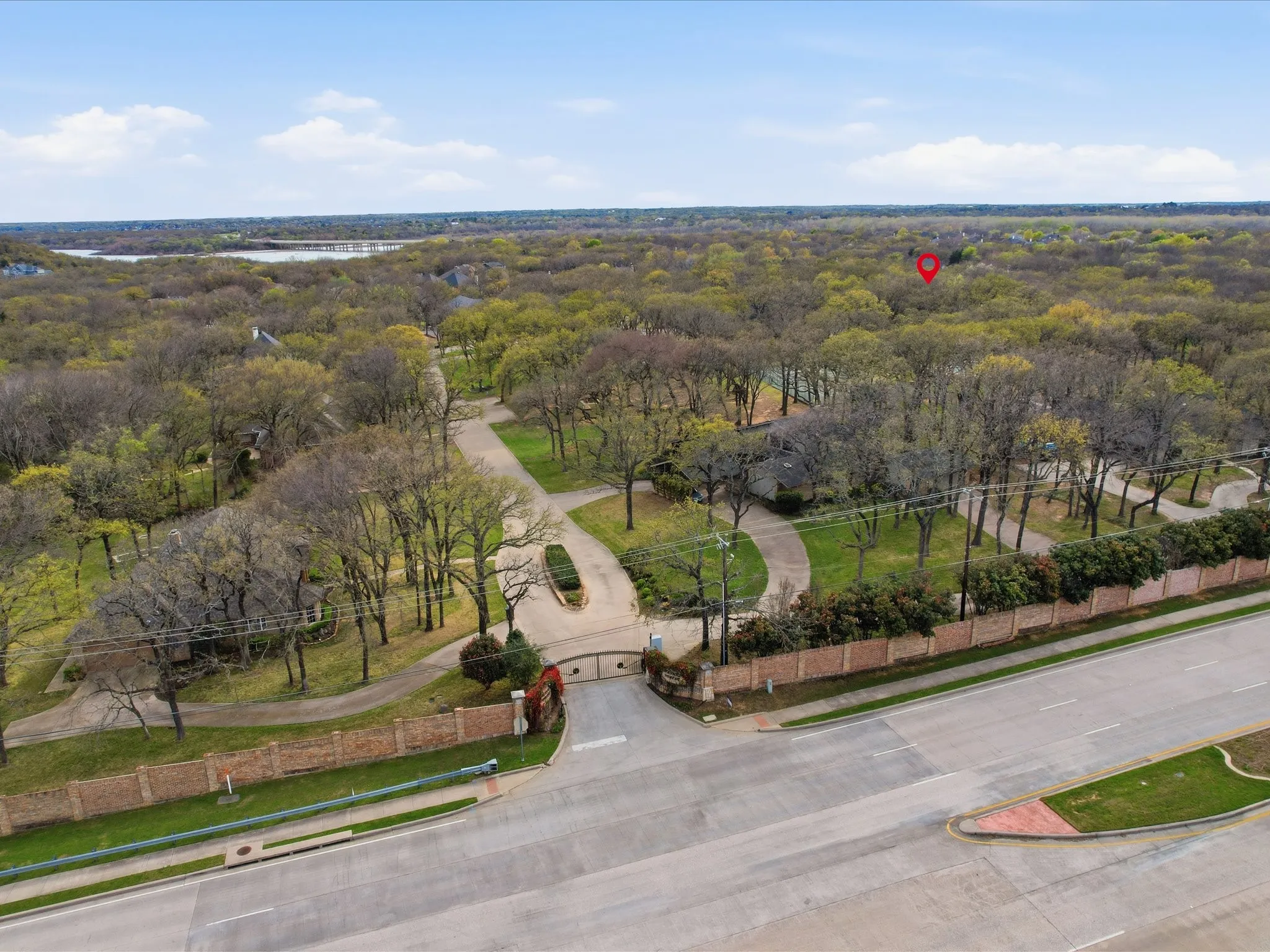 Aerial perspective of a gated entrance with brick perimeter wall, concrete driveway, and mature landscaping