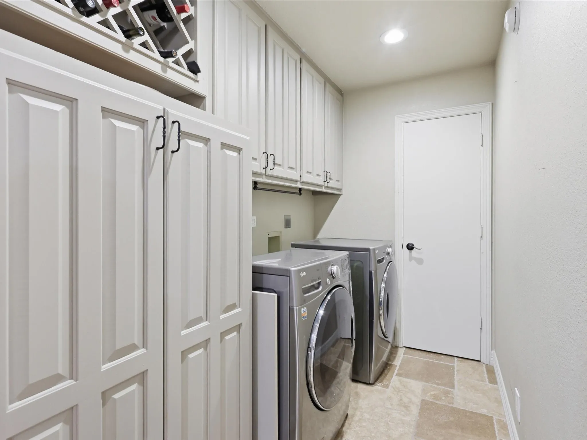 Custom cabinetry with integrated wine storage, upper and lower storage units, and stone-tile flooring