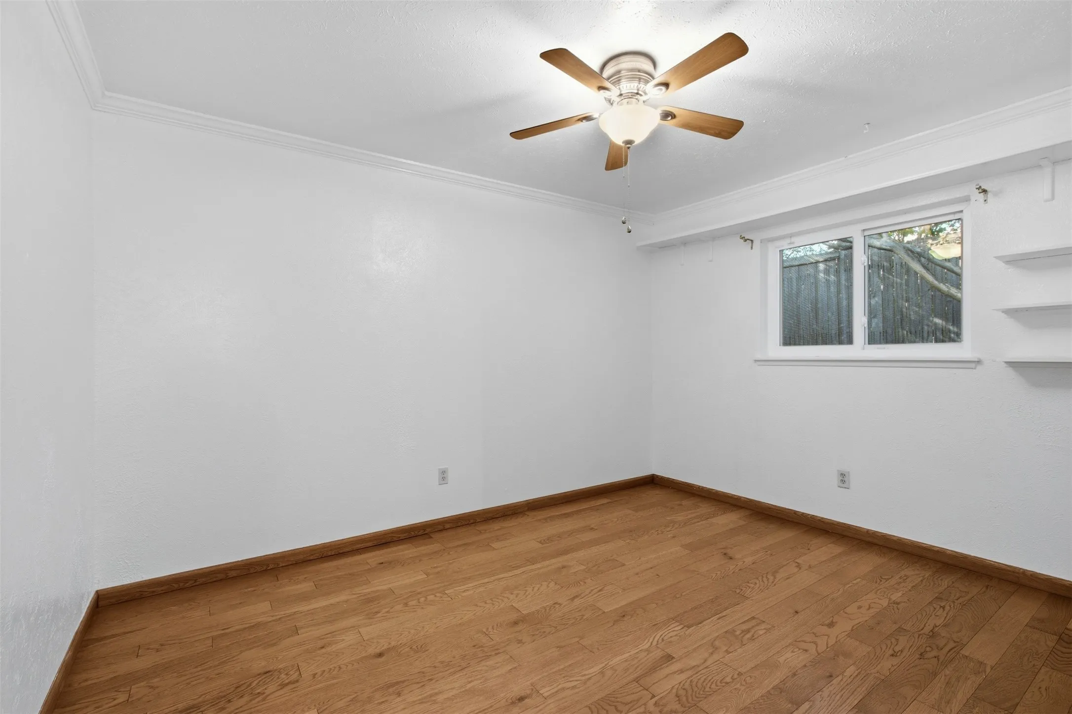Wood-finish flooring, crown molding, ceiling fan with integrated lighting, and built-in shelving