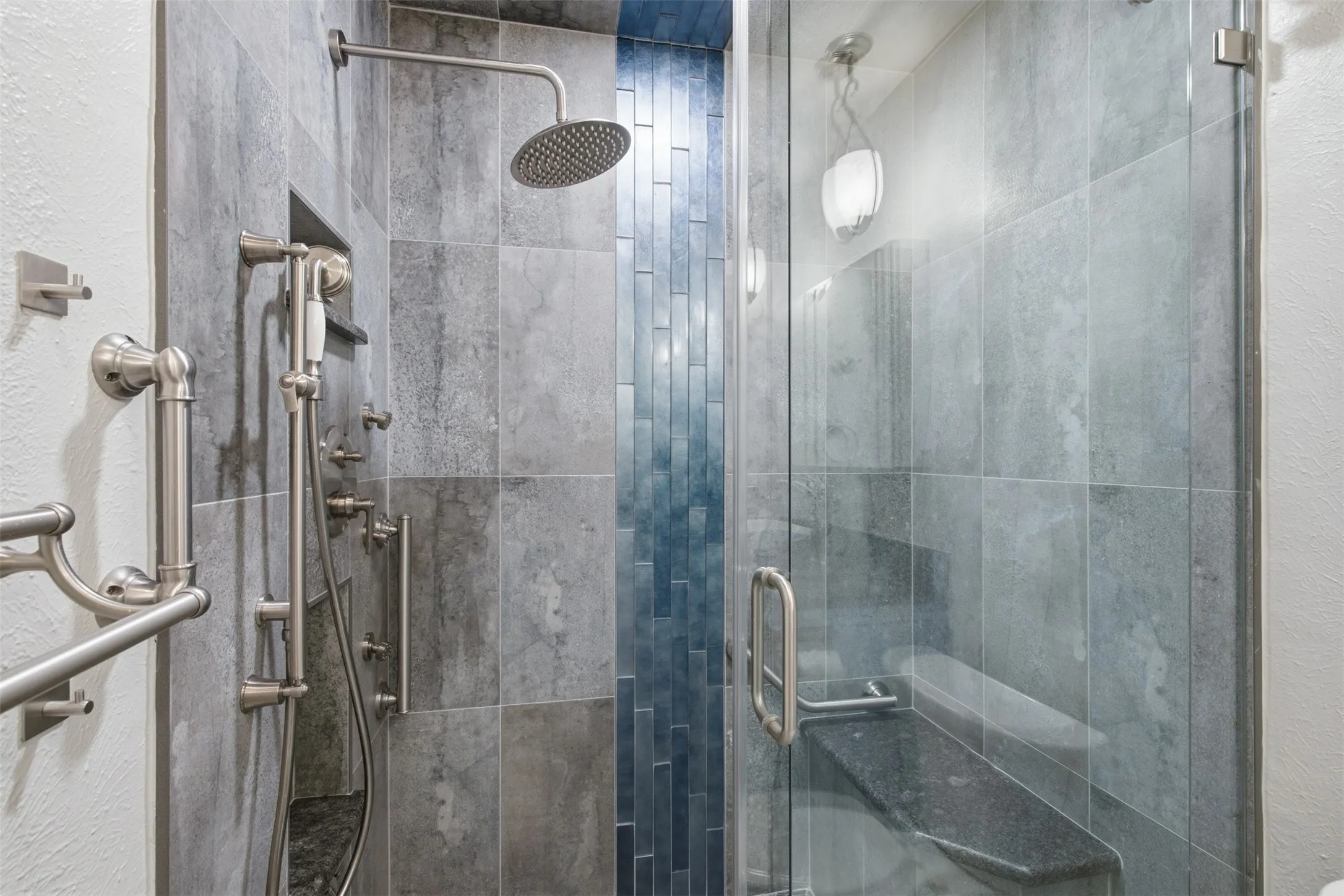 Glass-enclosed shower with a rainfall showerhead, handheld sprayer, and built-in bench