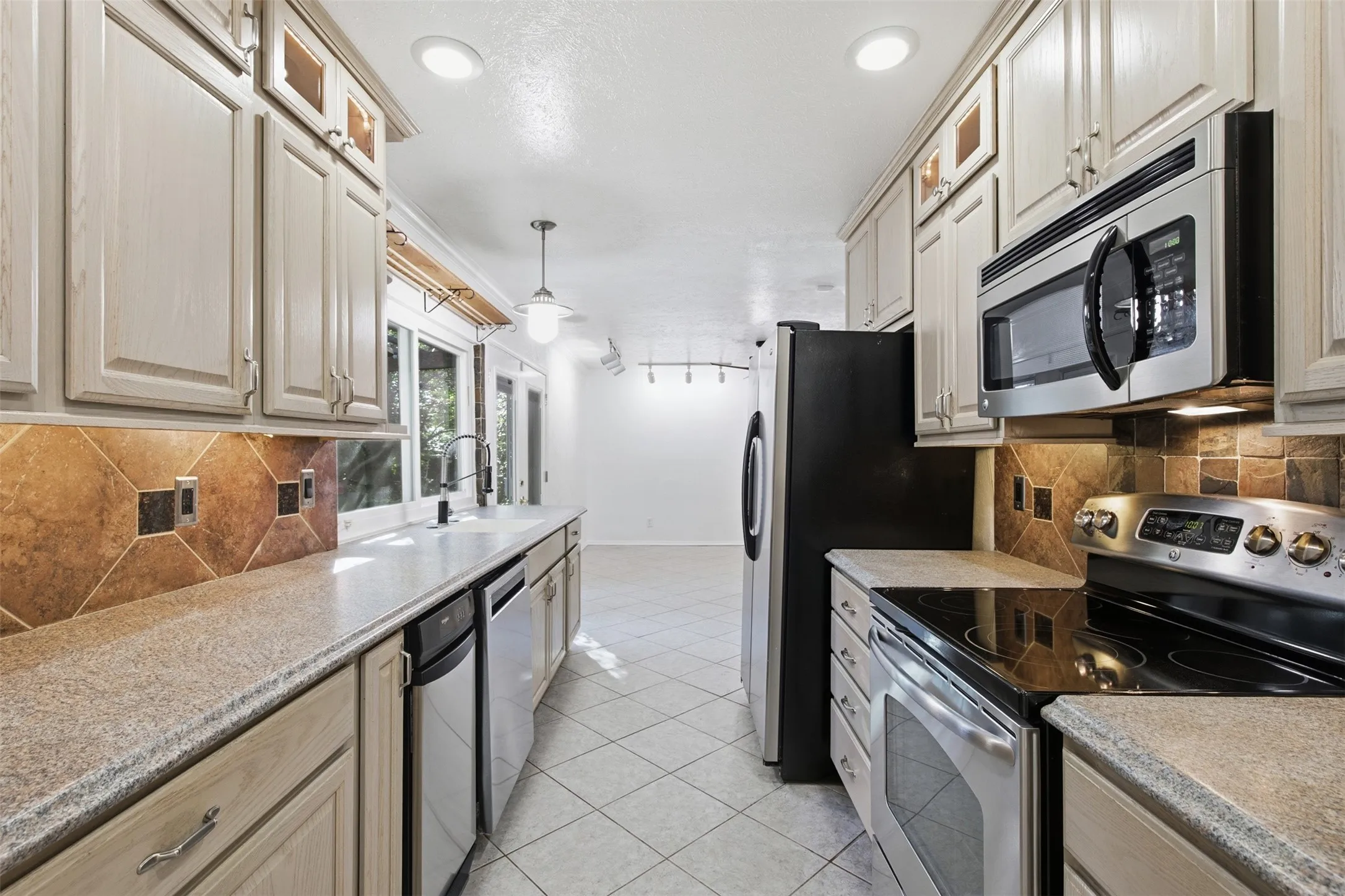 Galley kitchen featuring light-toned cabinetry, tile flooring, and integrated stainless steel appliances