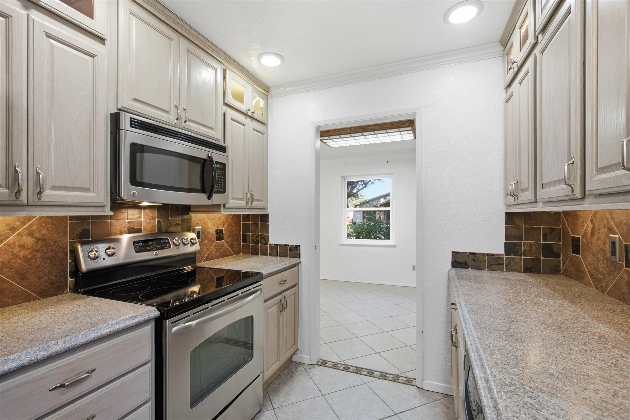 Stainless steel appliances, recessed lighting, tile backsplash, and light-toned cabinetry