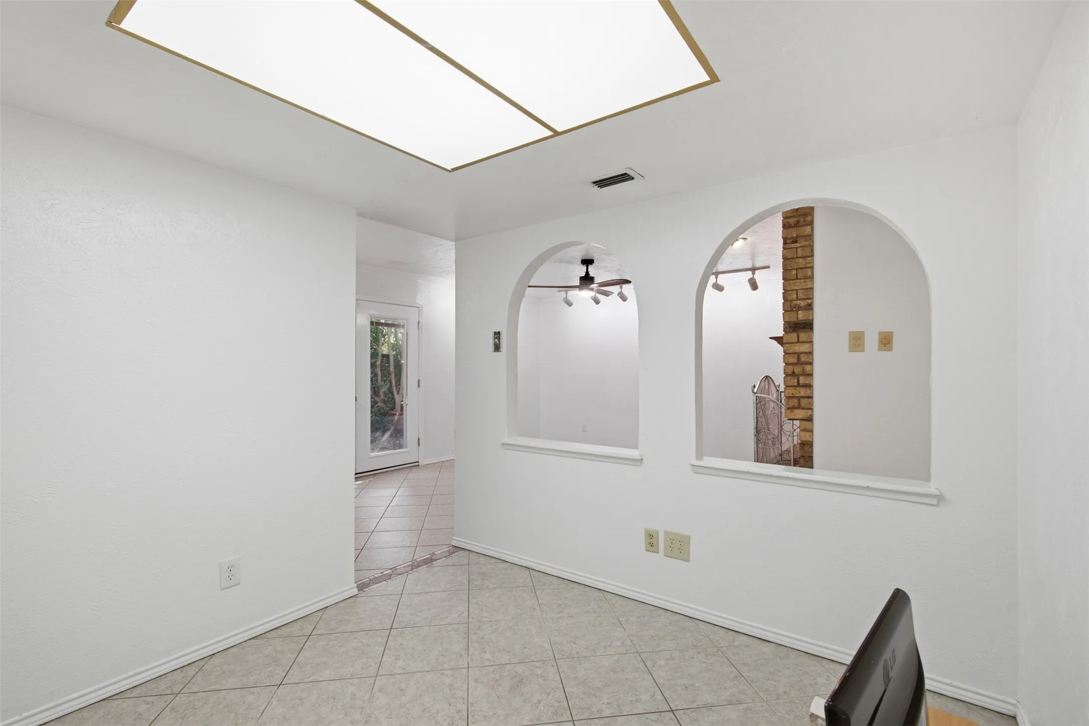 Recessed ceiling light panel, tiled flooring, two arched wall cutouts, brick accent wall, and a rear exterior door with glass paneling