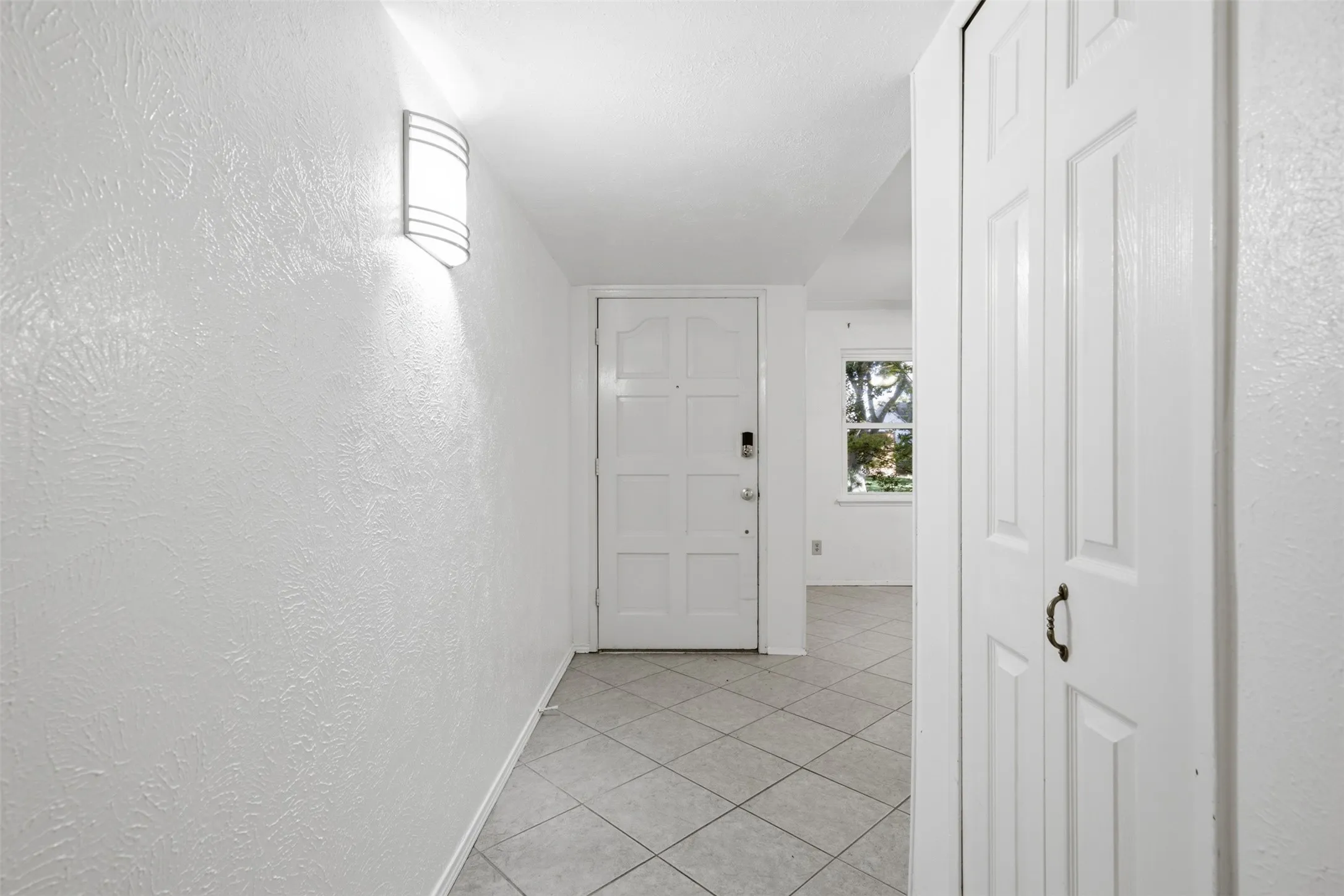 Textured wall finish, wall-mounted light fixture, paneled entry door, tiled flooring, built-in closet with paneled doors
