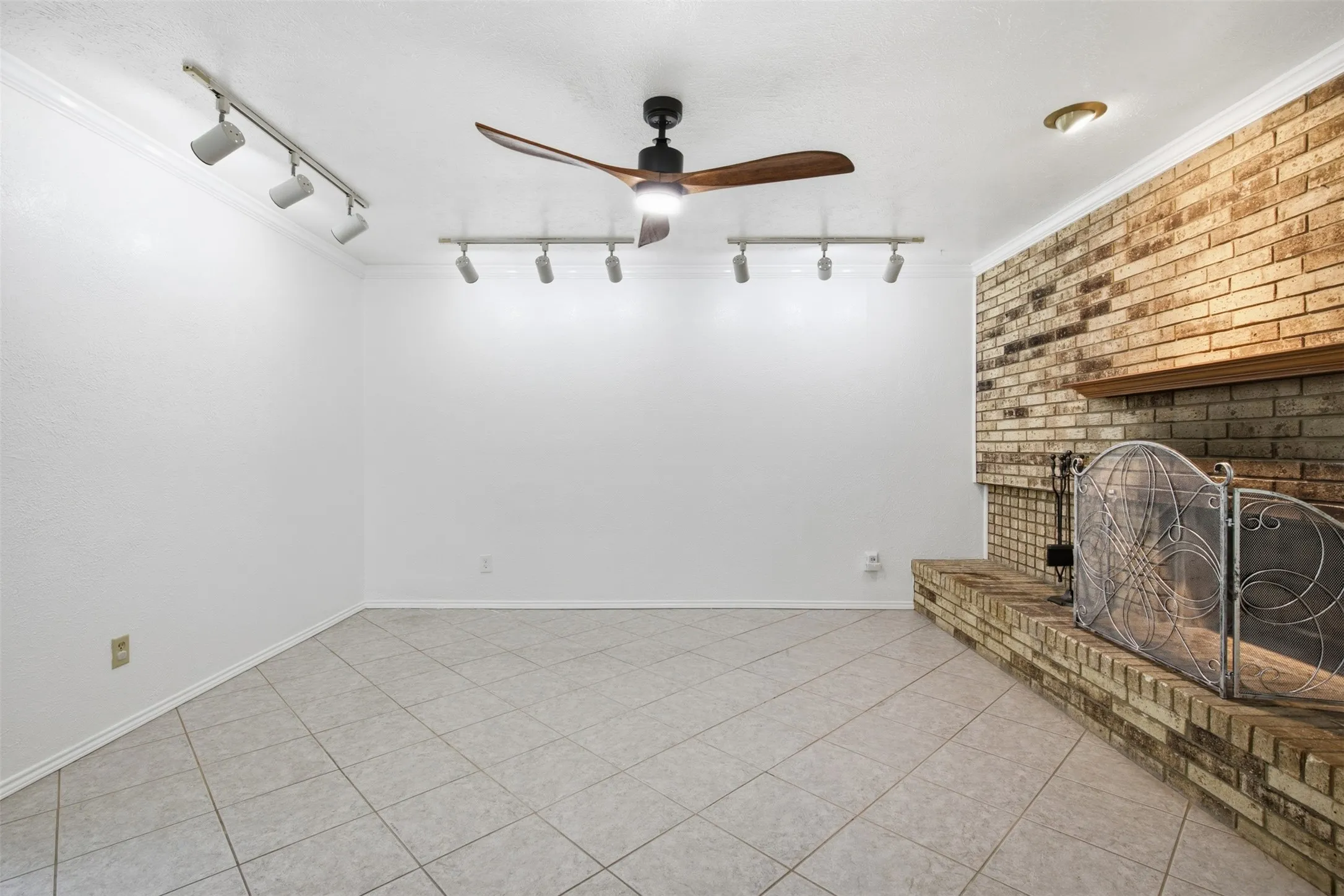 Brick fireplace with a wood mantle, tile flooring, ceiling fan, and track lighting fixtures