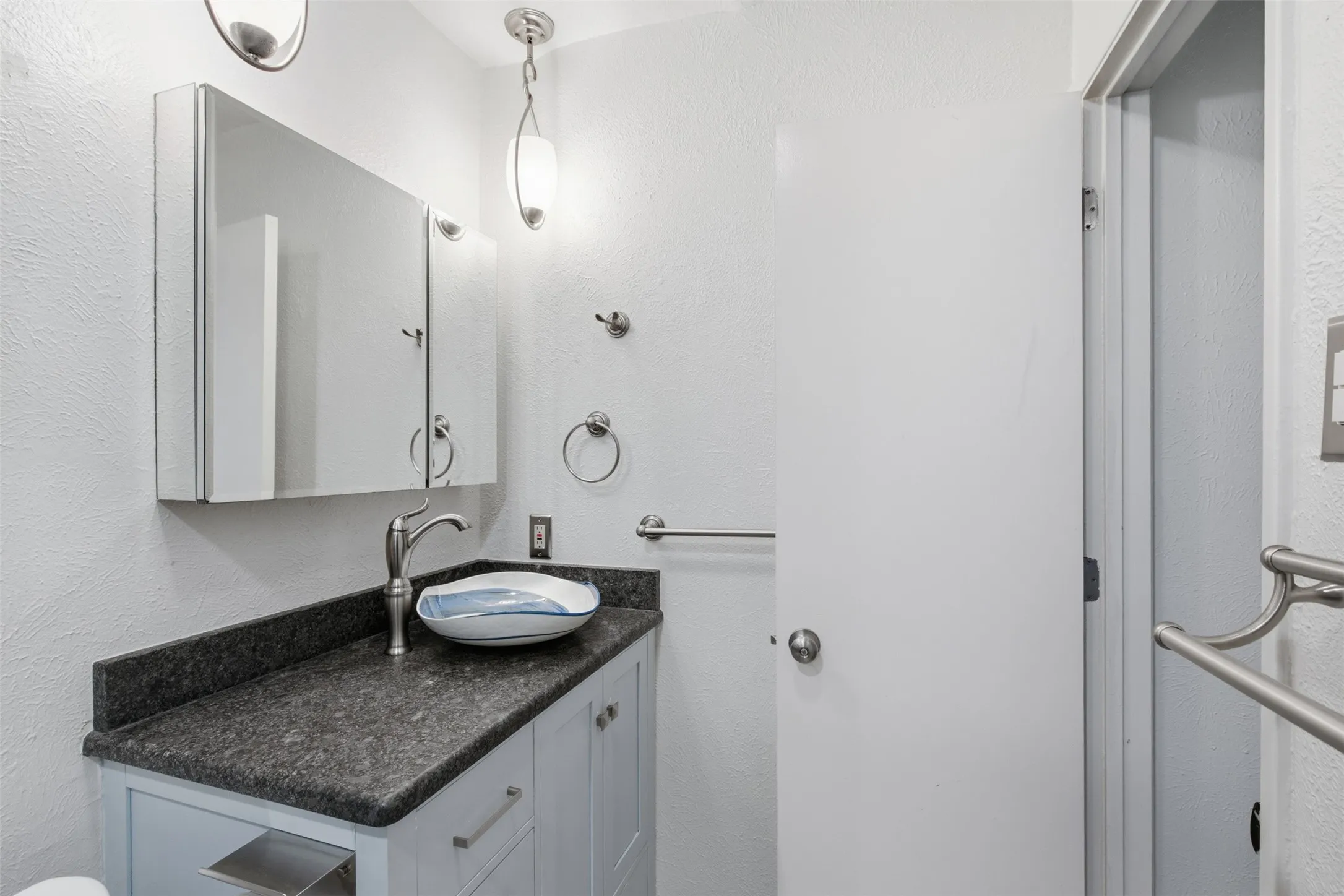 Vanity with dark countertop, vessel sink, and brushed nickel fixtures