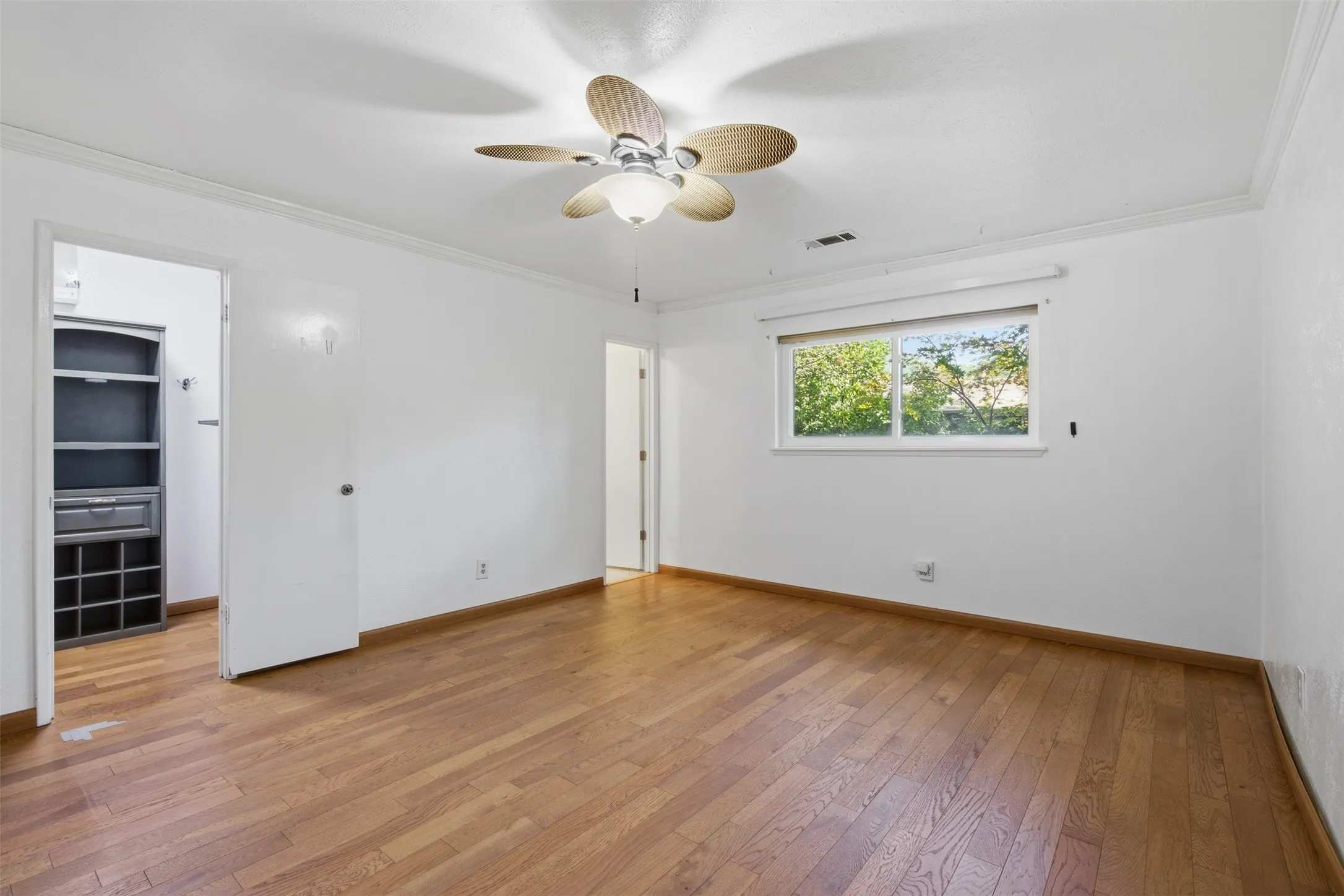 Wood-finish flooring, white walls, built-in closet organization system, ceiling fan with integrated lighting, and a window providing natural illumination