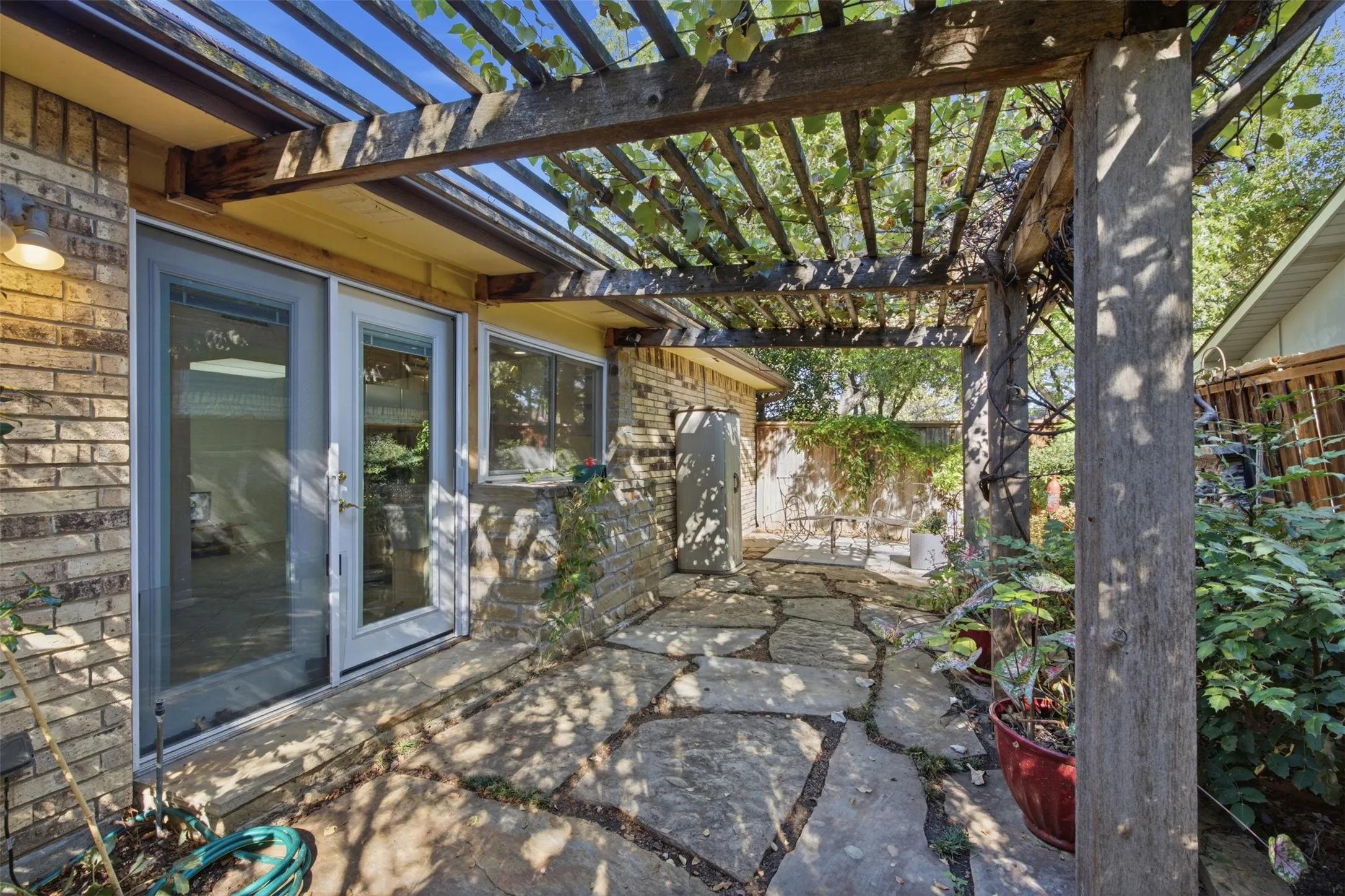 Stone patio with a wood pergola, brick exterior, and full-light glass doors