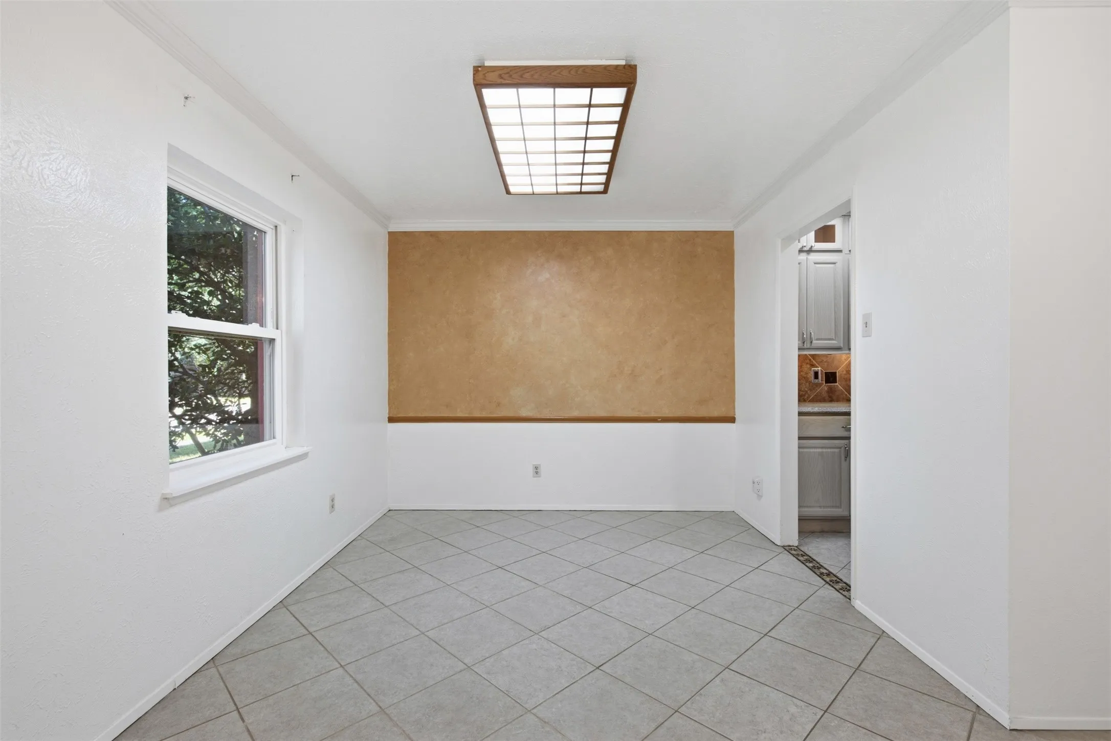 White interior walls with a textured accent wall, tile flooring, window with exterior landscaping, and a recessed ceiling light fixture