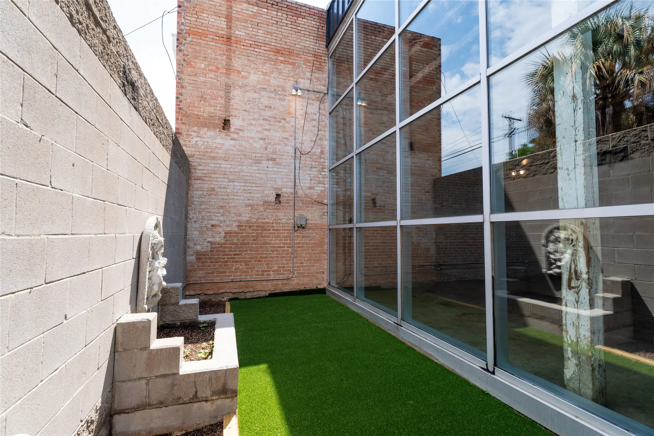 Exposed brick masonry walls, floor-to-ceiling glass paneling, concrete block privacy walls, and turf ground cover
