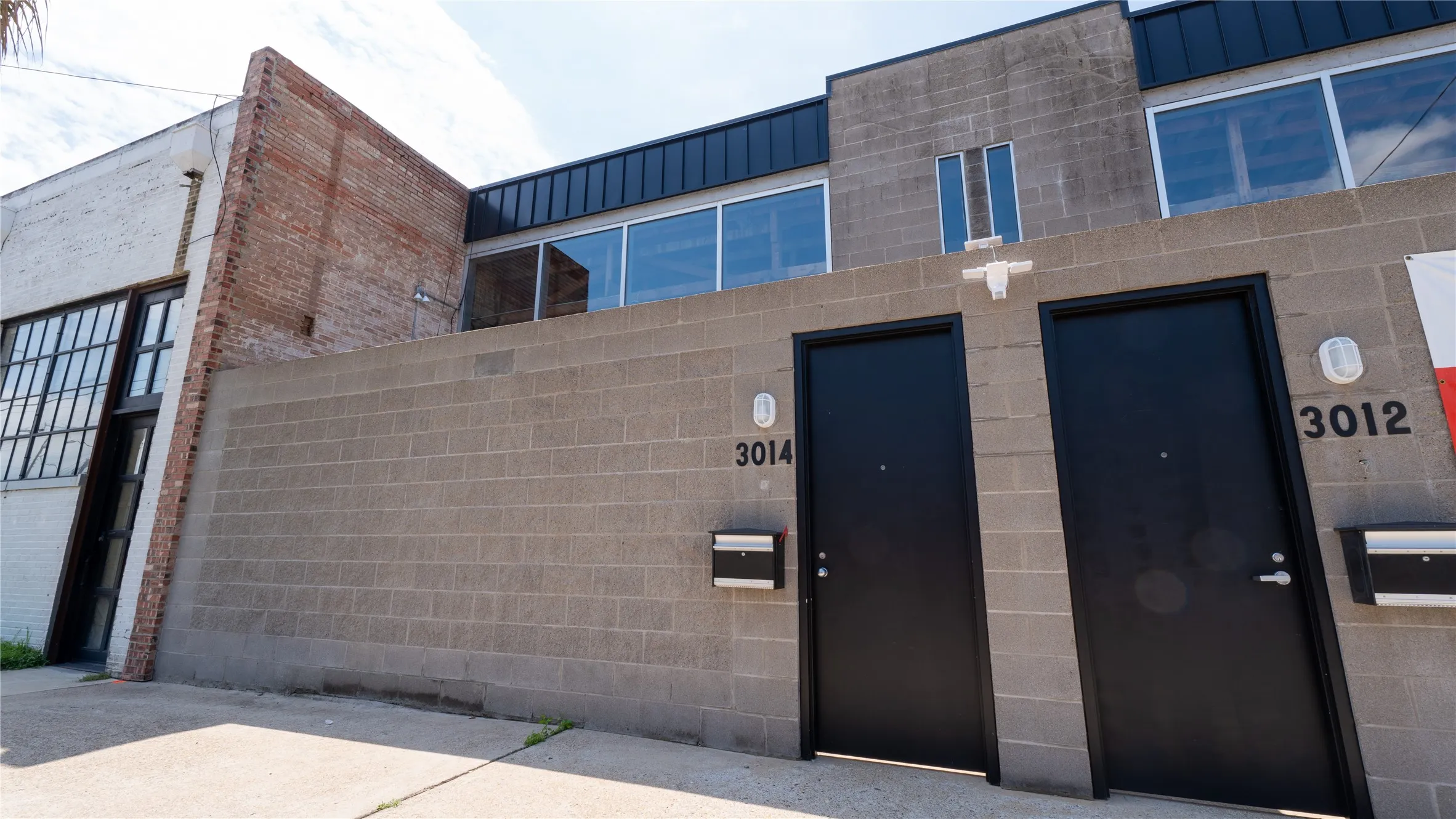 Industrial exterior featuring masonry walls, large-format glass window panels, flat roofing, and modern metal entry doors