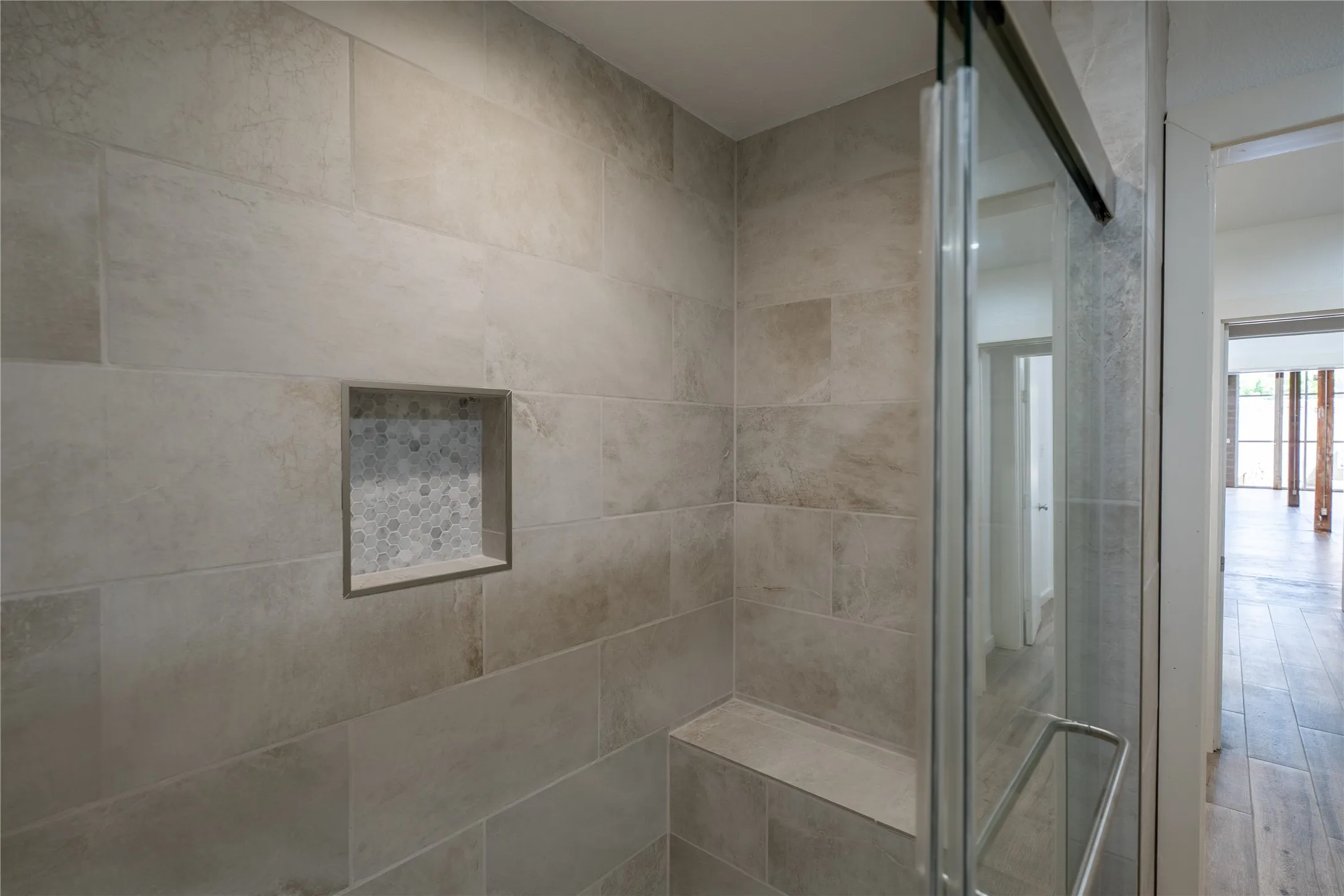 Walk-in shower featuring large-format neutral wall tile, integrated tiled bench, inset mosaic-tiled wall niche, and glass enclosure