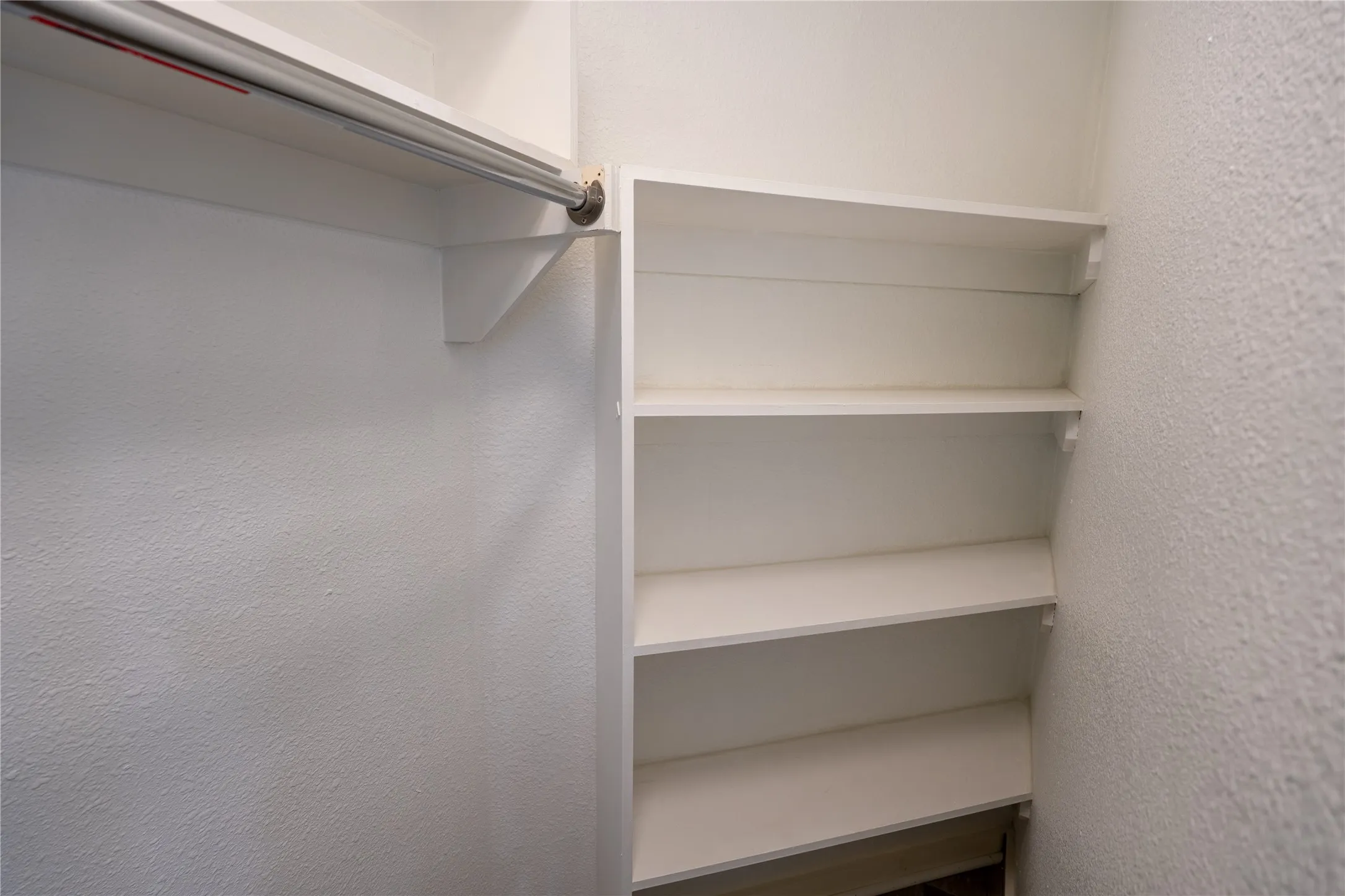 Built-in white shelving unit featuring four storage tiers and a wall-mounted metal garment rod with overhead shelf