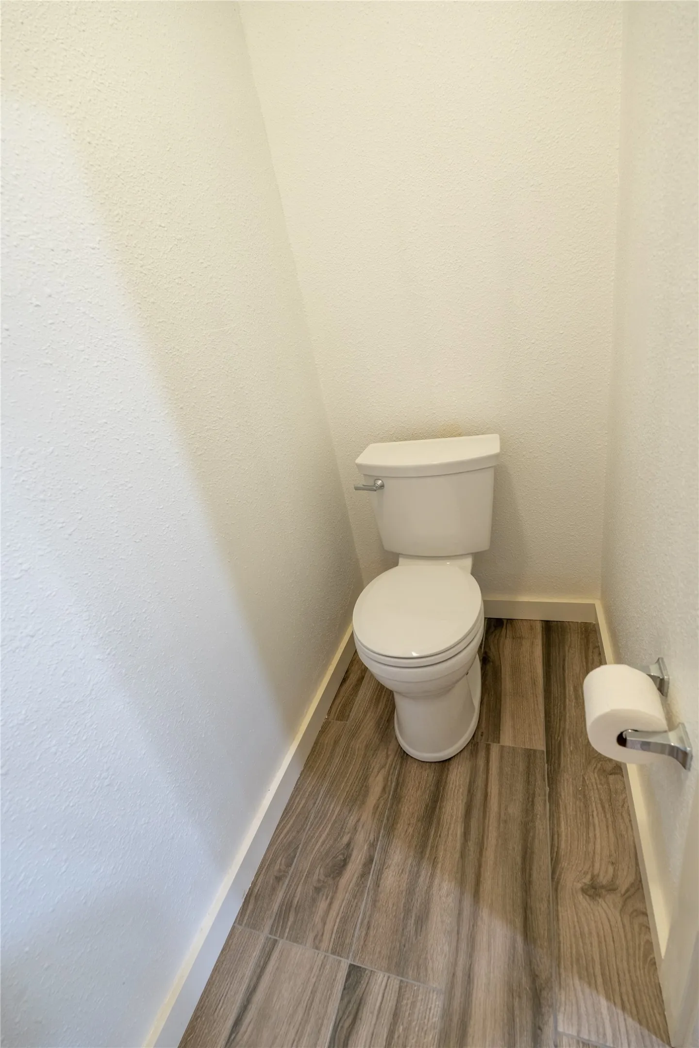 Standard-height porcelain toilet paired with wood-finish flooring and a chrome toilet paper holder
