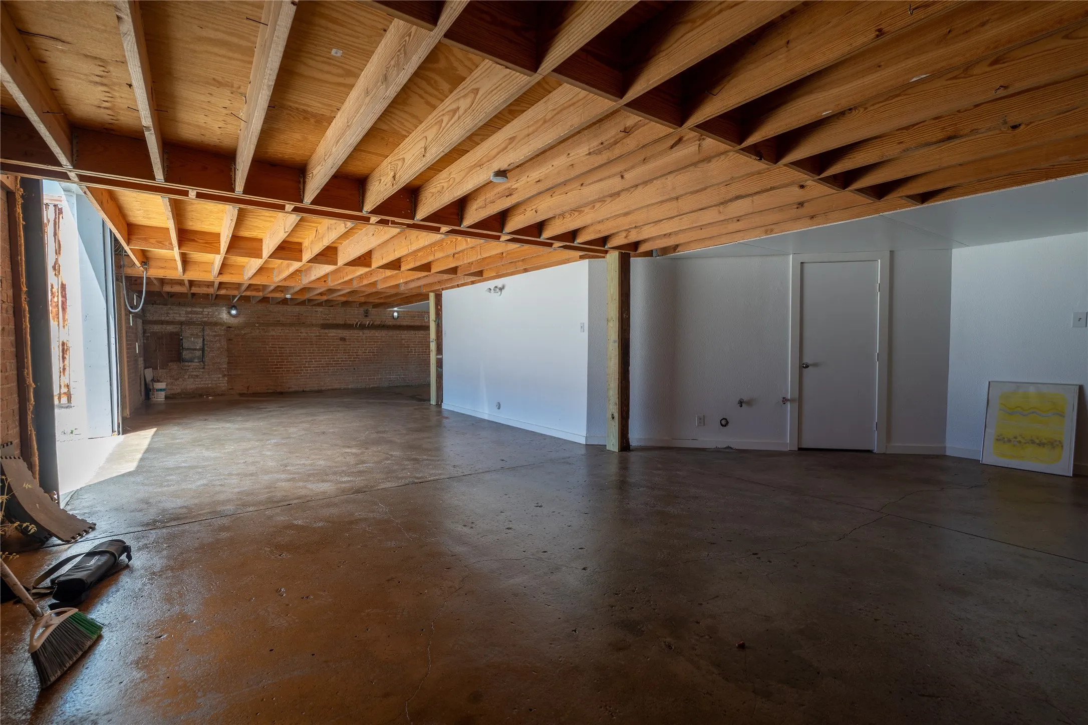 Expansive lower level featuring exposed wood joist ceilings, polished concrete flooring, white walls, and a structural timber support column