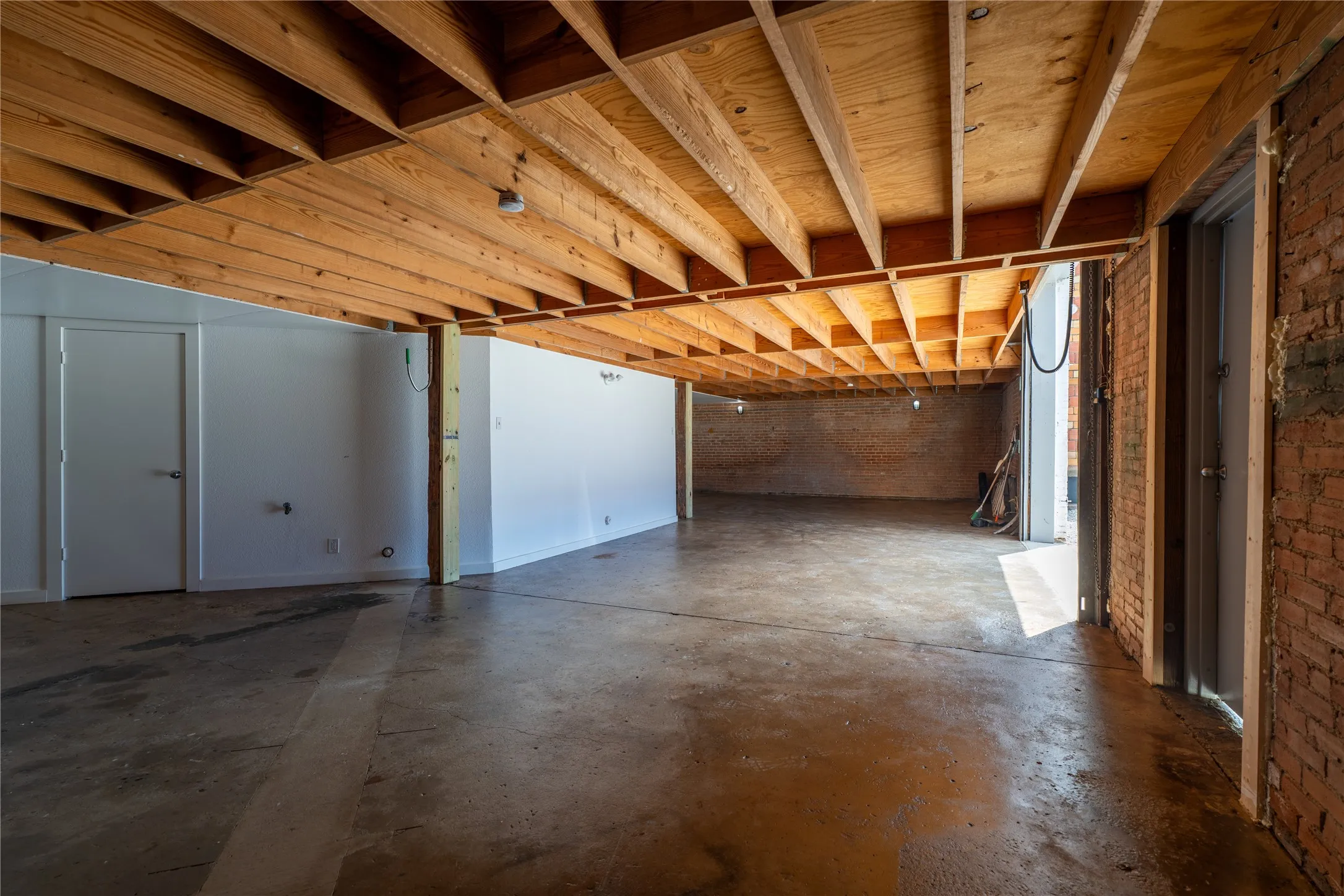 Industrial-style interior featuring exposed wooden ceiling joists, concrete flooring, exposed brick wall segments, and painted white wall finishes