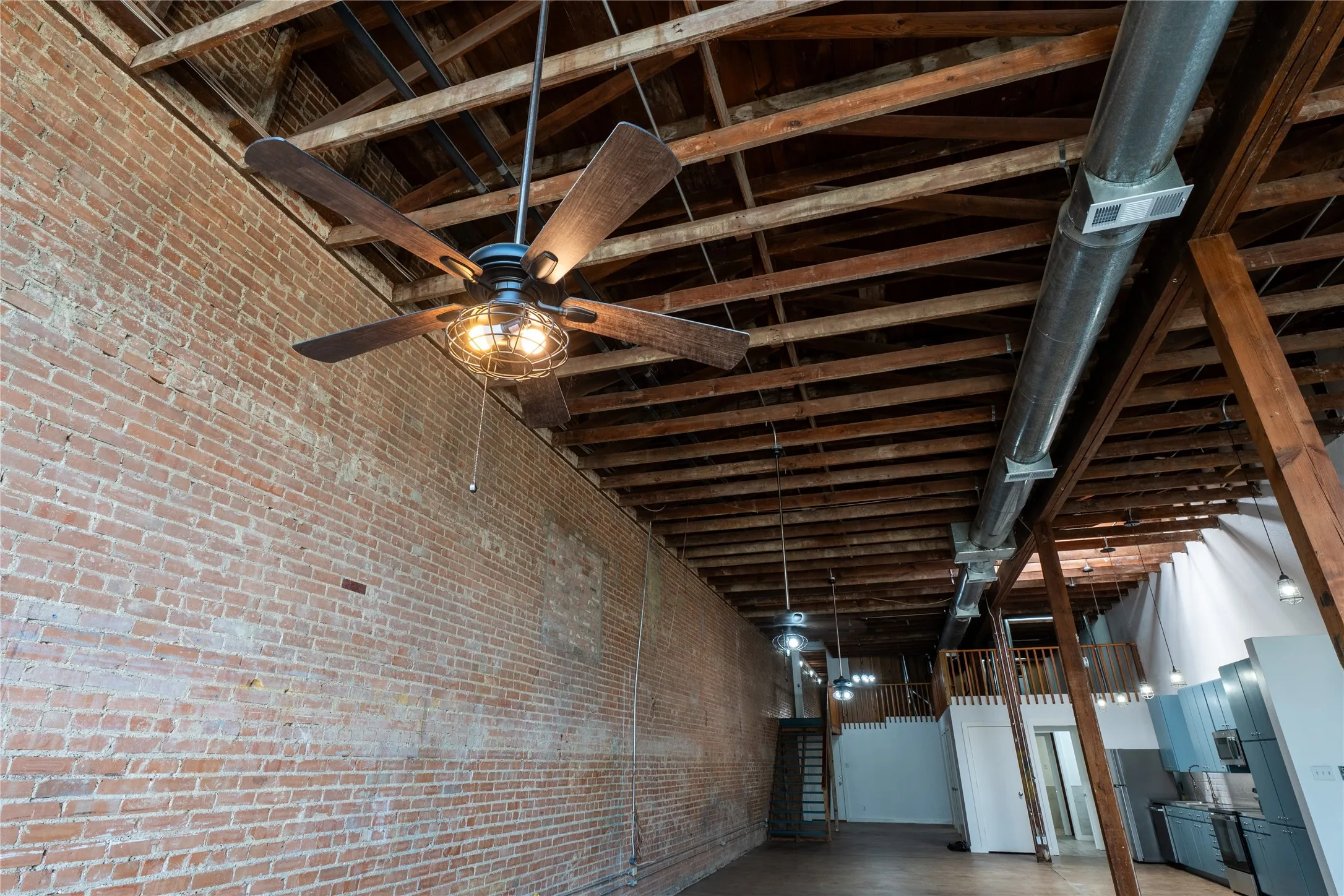 Industrial interior featuring exposed brick walls, vaulted timber-beam ceilings, exposed ductwork, and suspended cage-style ceiling fans