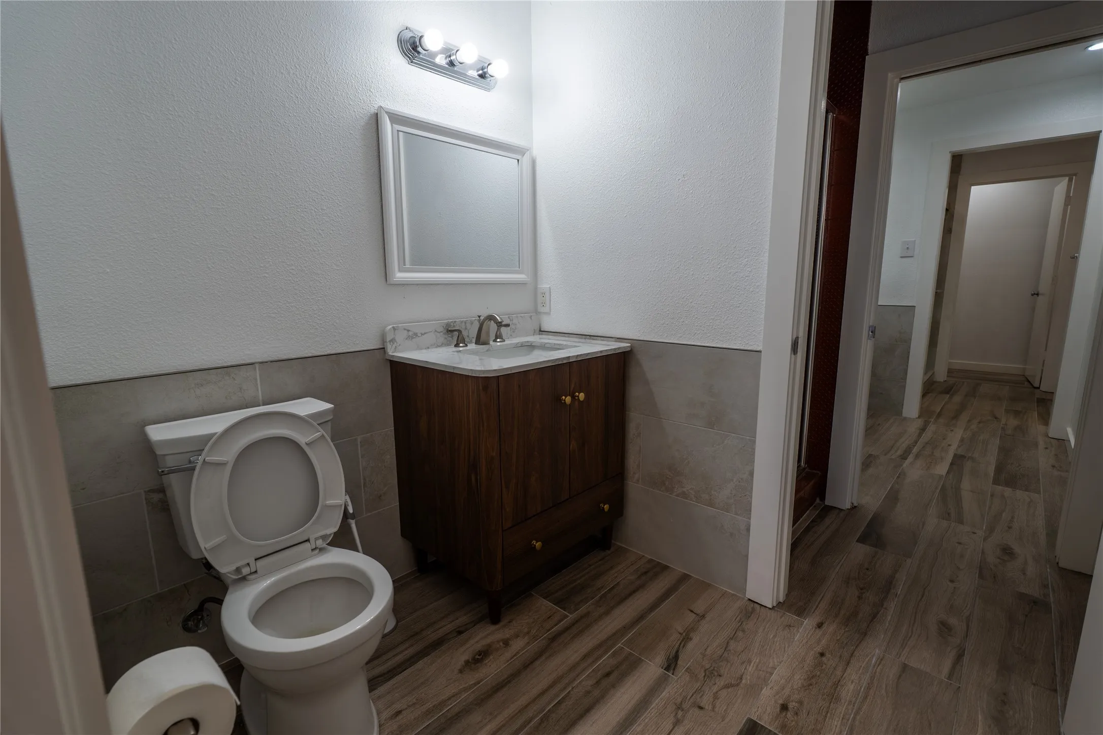Bathroom featuring wood-finish cabinetry, a stone-composite countertop, light-toned wall tile wainscoting, and wood-finish flooring