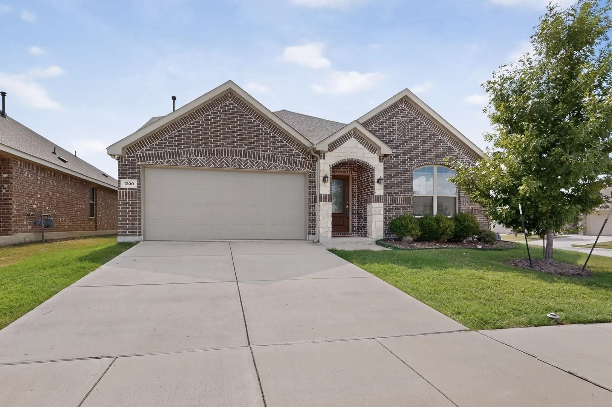 Single-story residence featuring a brick and stone facade, dual gables, an arched entryway, and a concrete driveway leading to a two-car garage