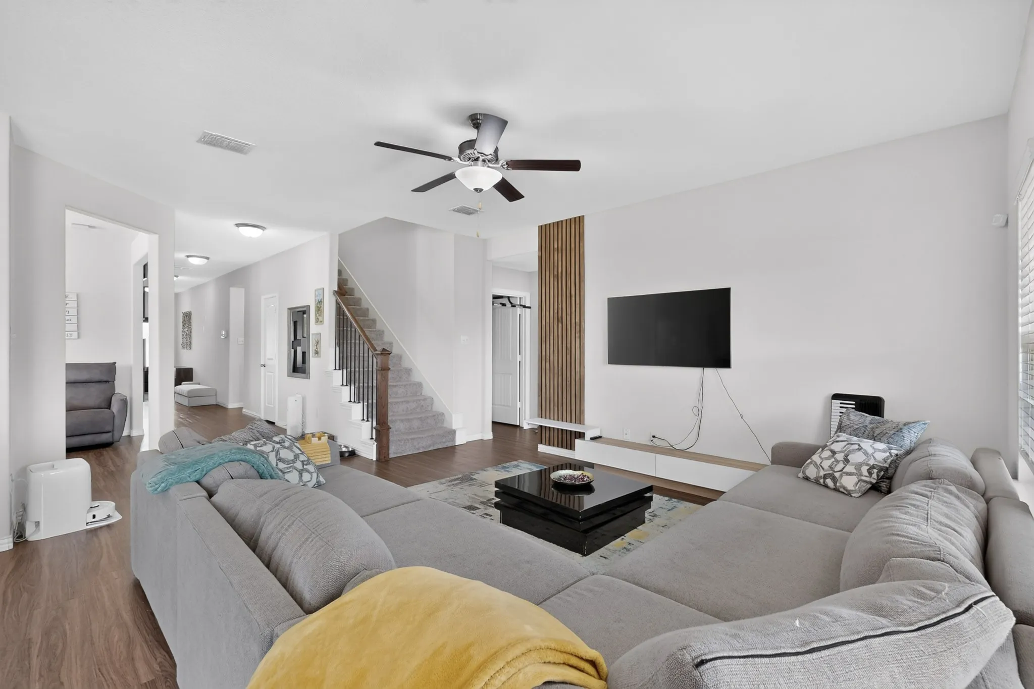 Living area featuring wood-finish flooring, a vertical wood slat accent wall, a built-in low-profile media console, and a staircase with a wooden handrail and metal balusters