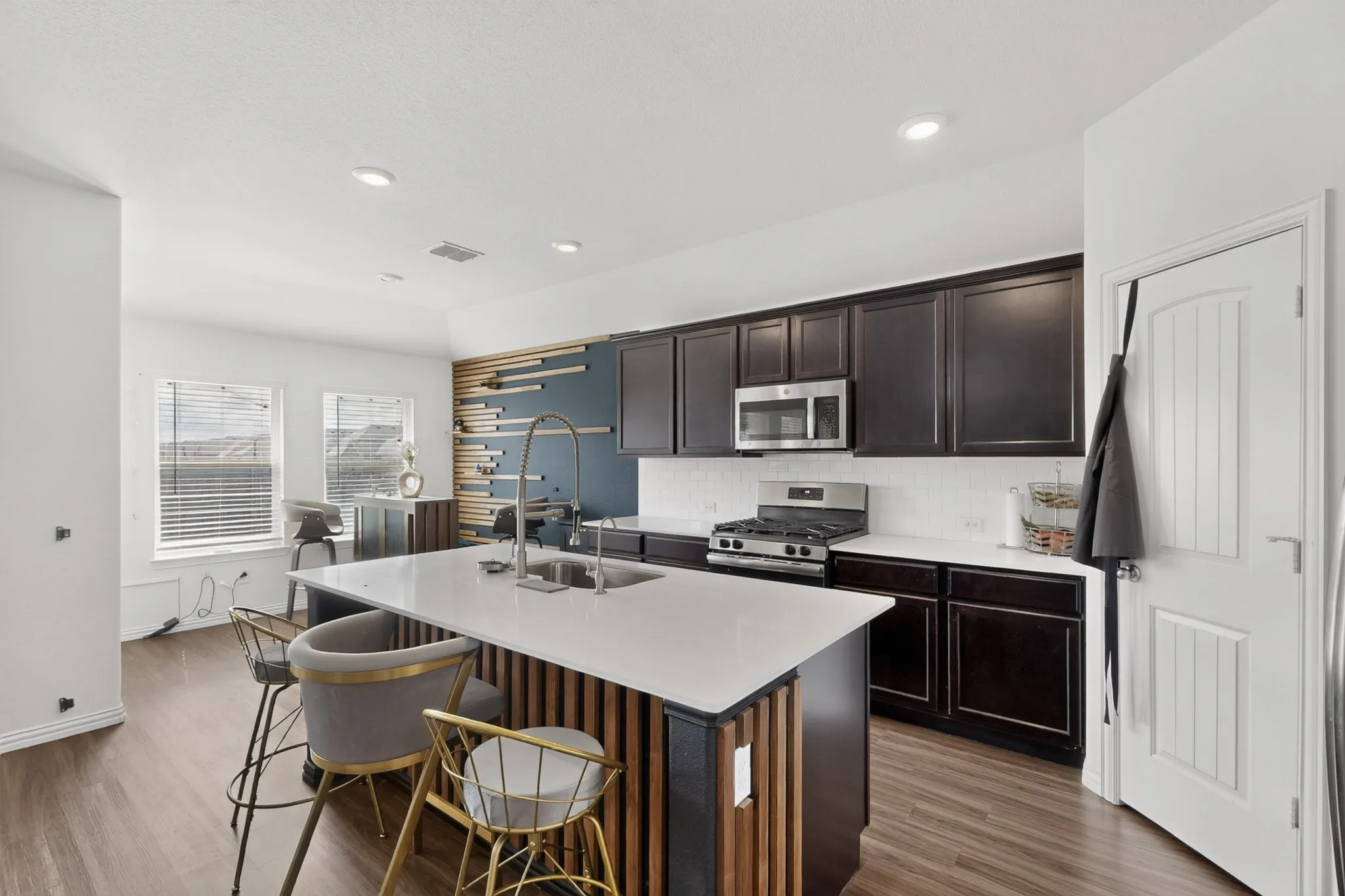 Kitchen featuring dark cabinetry, solid-surface countertops, center island with vertical wood-slat detailing, stainless steel gas range, and recessed lighting