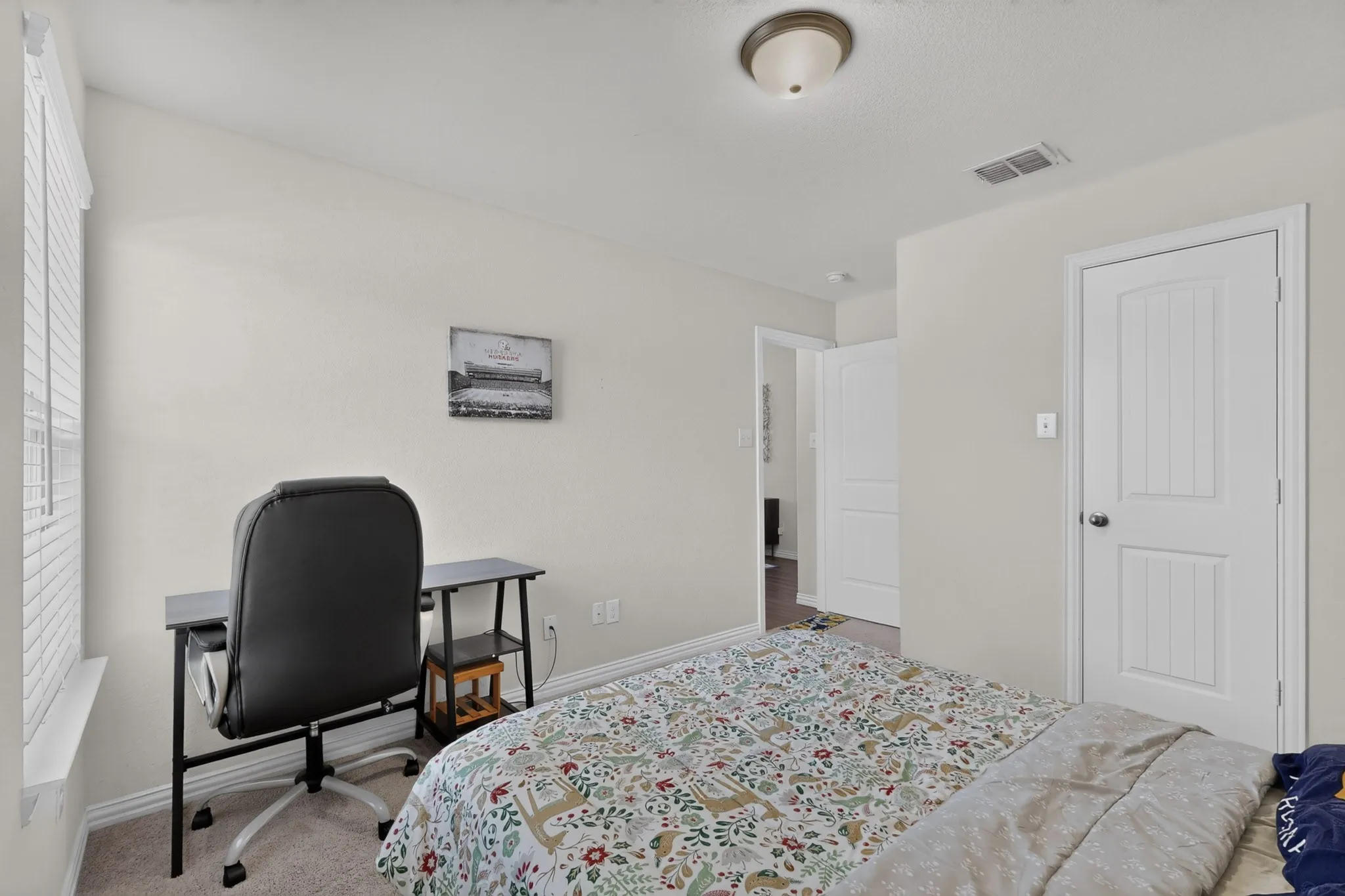 Neutral-toned interior room featuring wall-to-wall carpeting, a multi-panel interior door, horizontal slat window blinds, and a ceiling-mounted light fixture