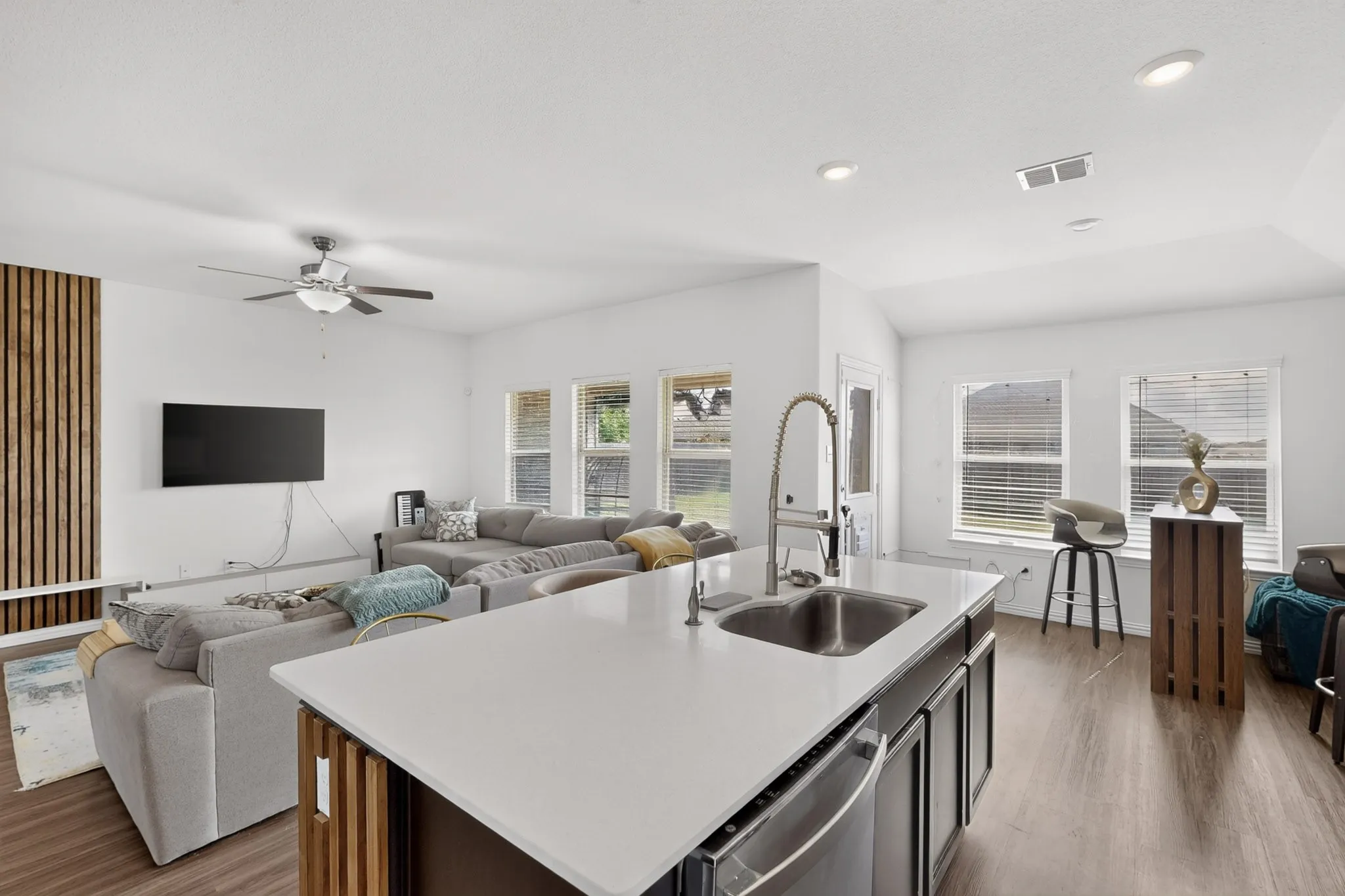 Kitchen island with solid-surface countertop, stainless steel undermount sink, and pull-down faucet, featuring a vertical wood-slat accent wall and wood-finish flooring throughout