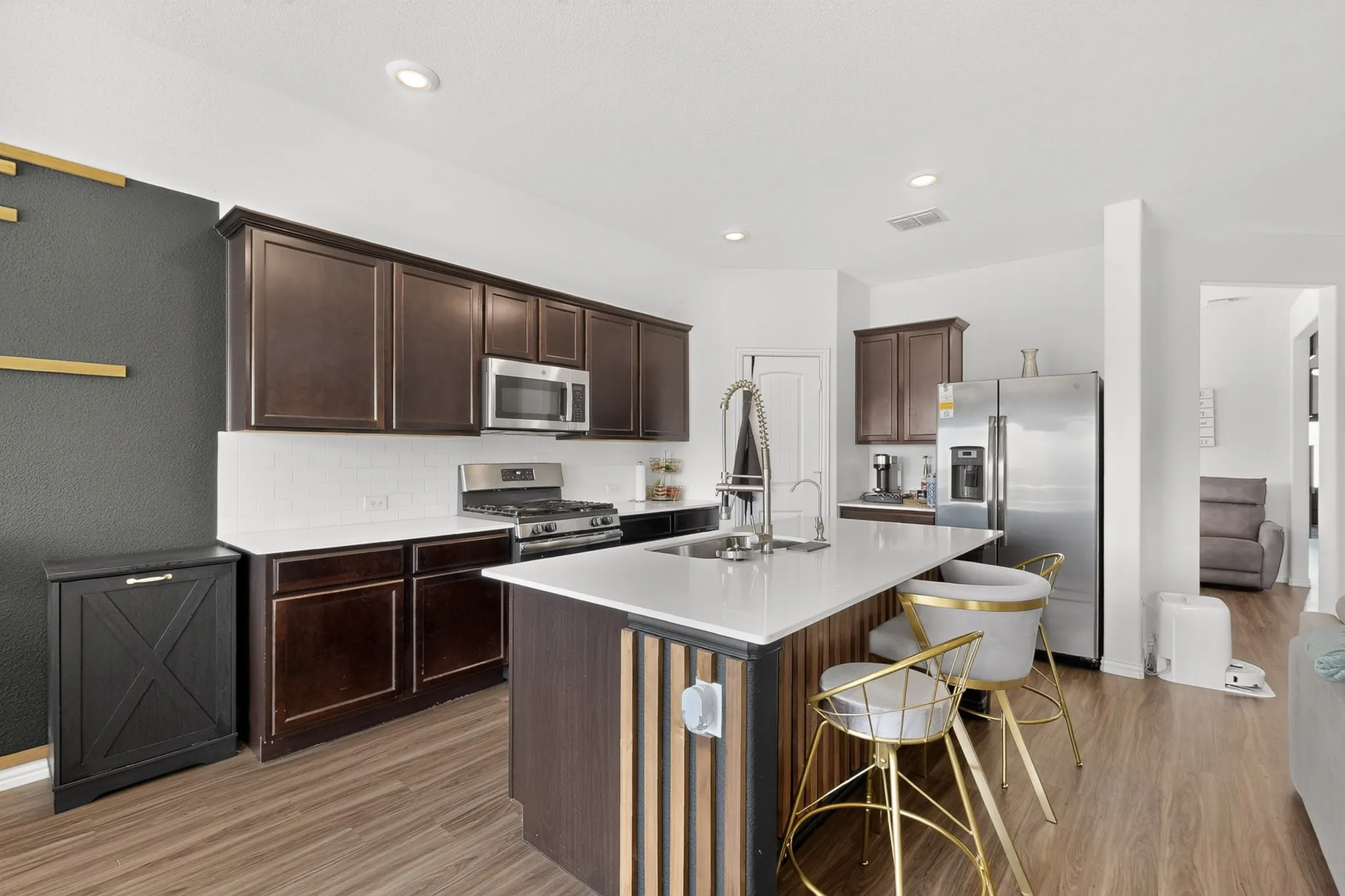 Kitchen featuring dark cabinetry, solid-surface countertops, wood-finish flooring, stainless steel appliances, and a central island with vertical wood detailing