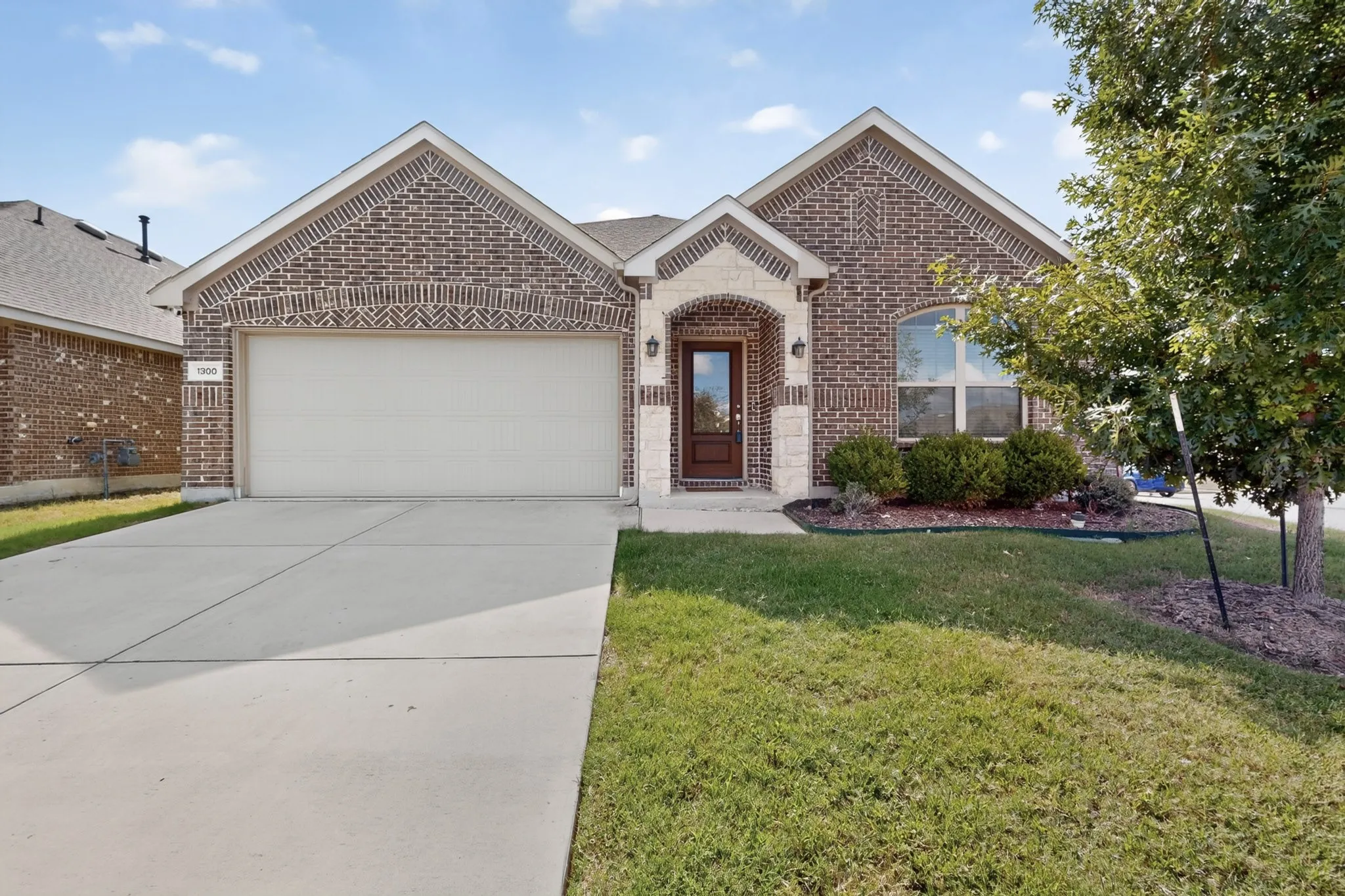 Traditional brick exterior featuring a stone-accented arched entryway, dual-gable roofline, and attached two-car garage