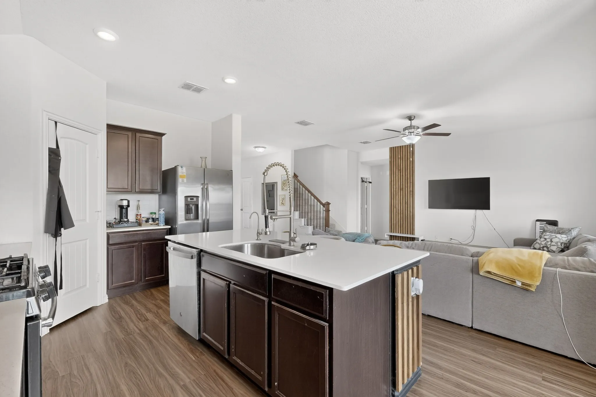 Kitchen island with a solid surface countertop, undermount stainless steel sink, pull-down faucet, wood-finish cabinetry, and wood-finish flooring