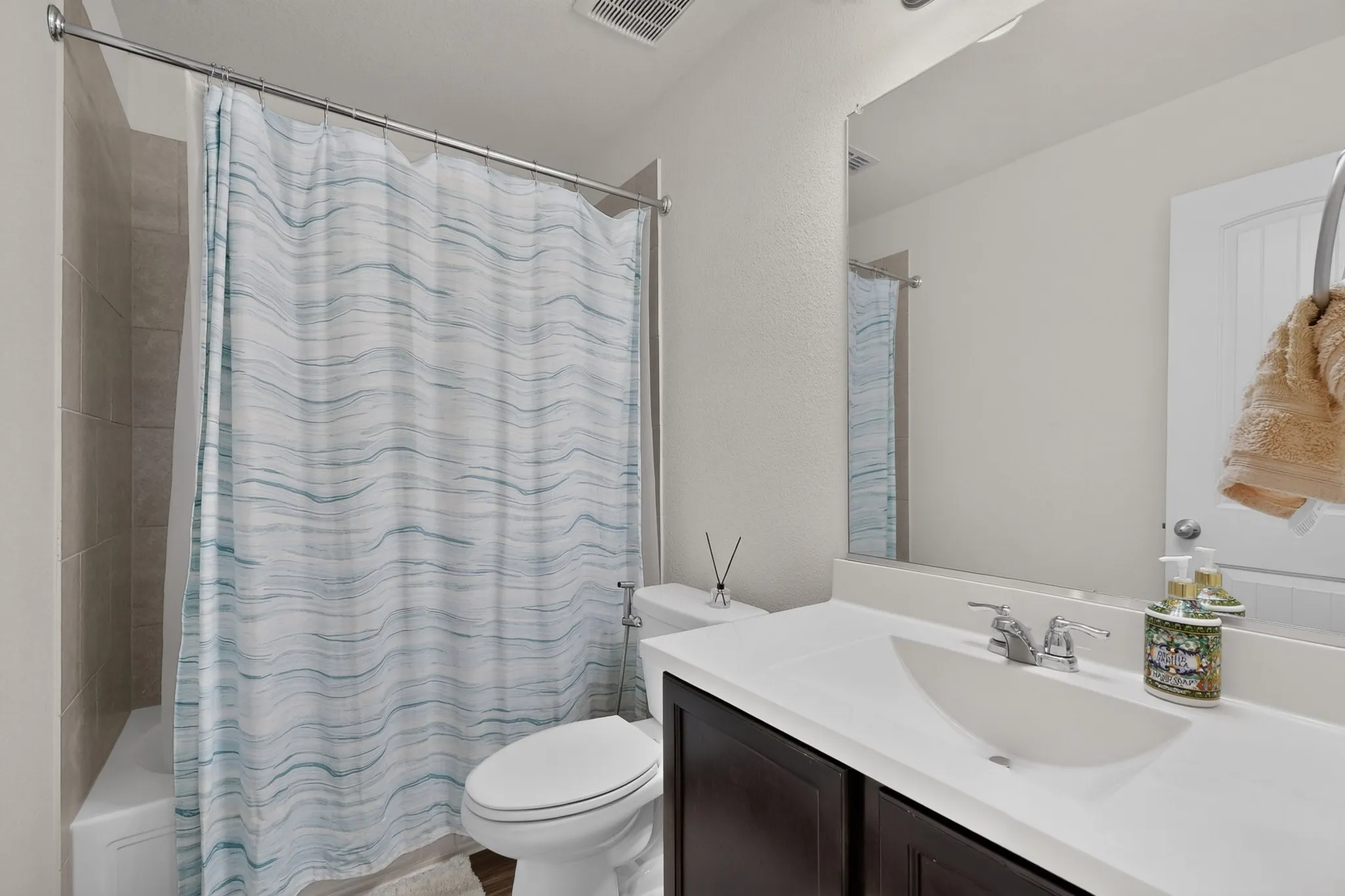 Bathroom featuring a dark-finish vanity with an integrated white sink, a wide wall-mounted mirror, and a tile-surround shower and tub combination