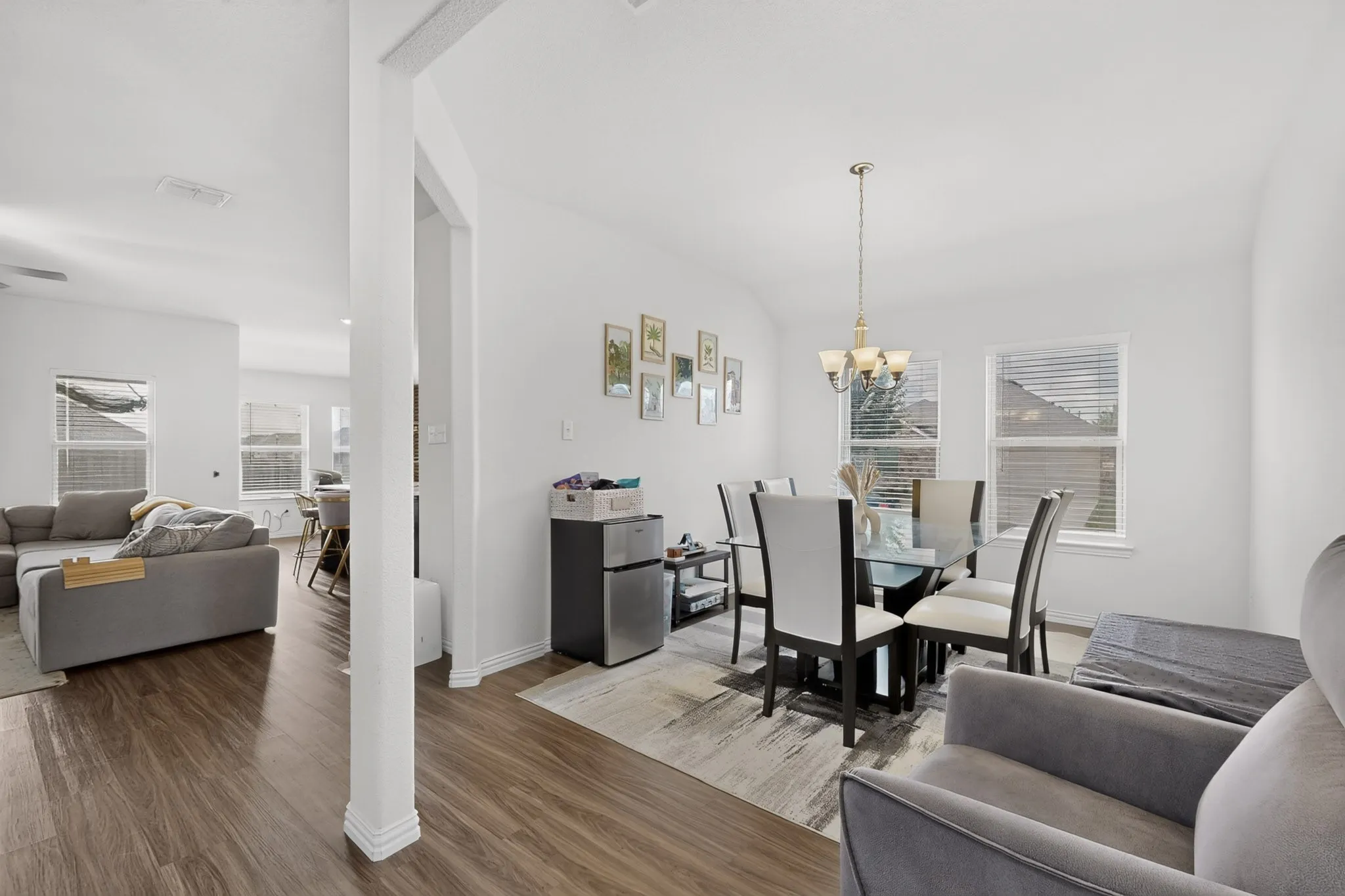 Open-concept area featuring wood-finish flooring, multi-pane windows with integrated blinds, and an overhead multi-light chandelier