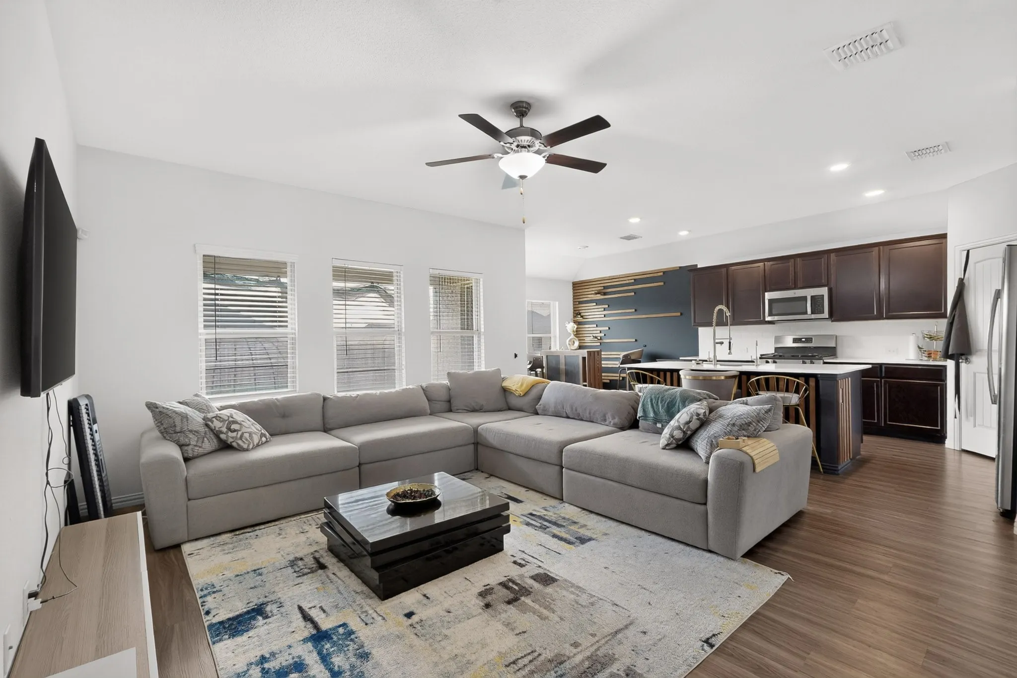 Open-concept space featuring wood-finish flooring, recessed lighting, a ceiling fan, and a kitchen equipped with dark-toned cabinetry, light-toned countertops, and stainless steel appliances