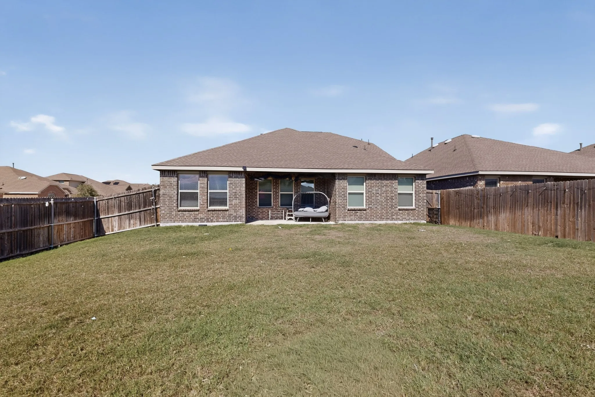 Brick exterior featuring a covered rear patio, expansive lawn, and full wood privacy fencing