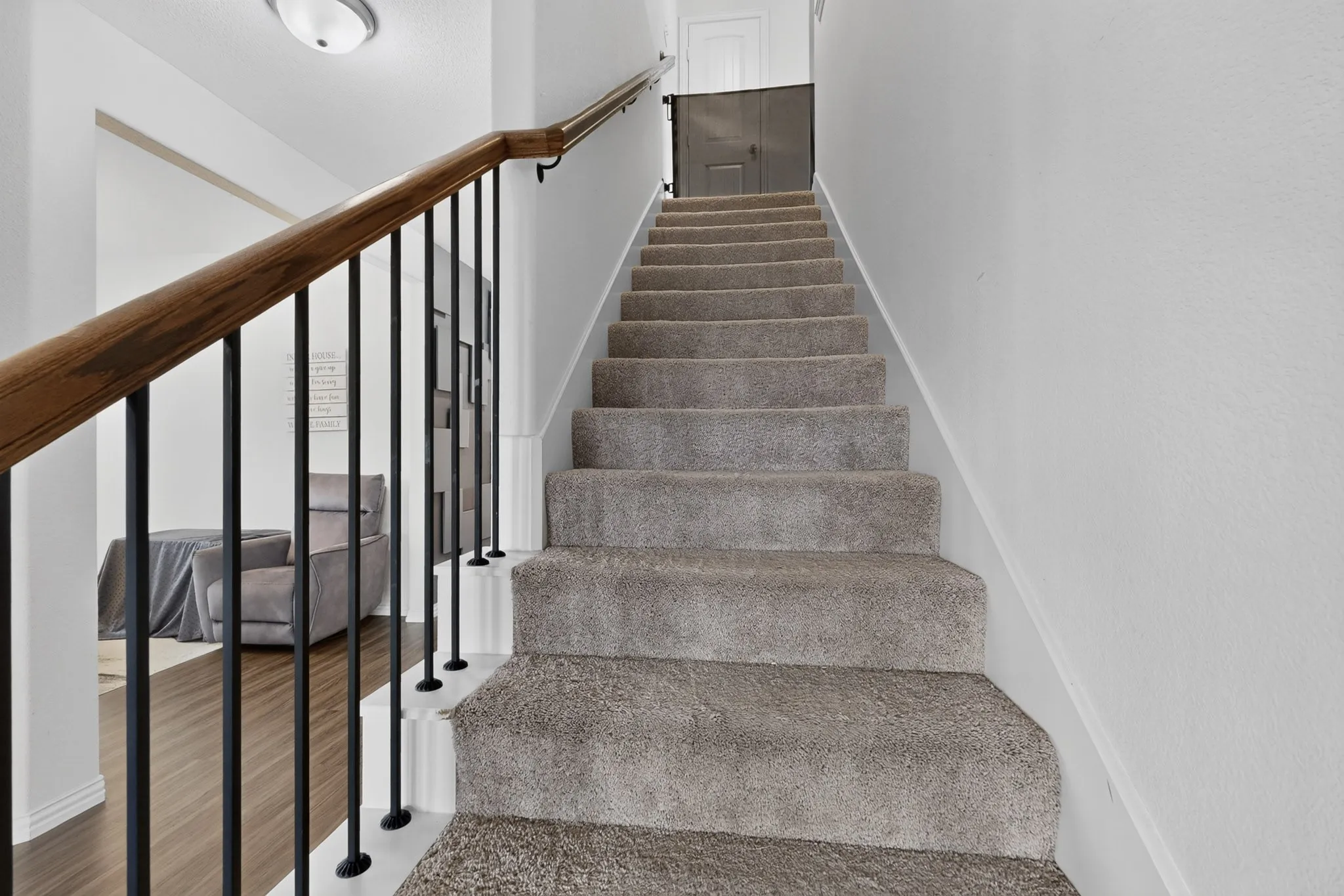 Staircase featuring plush carpeted treads, a wood-finish handrail, and black metal balusters