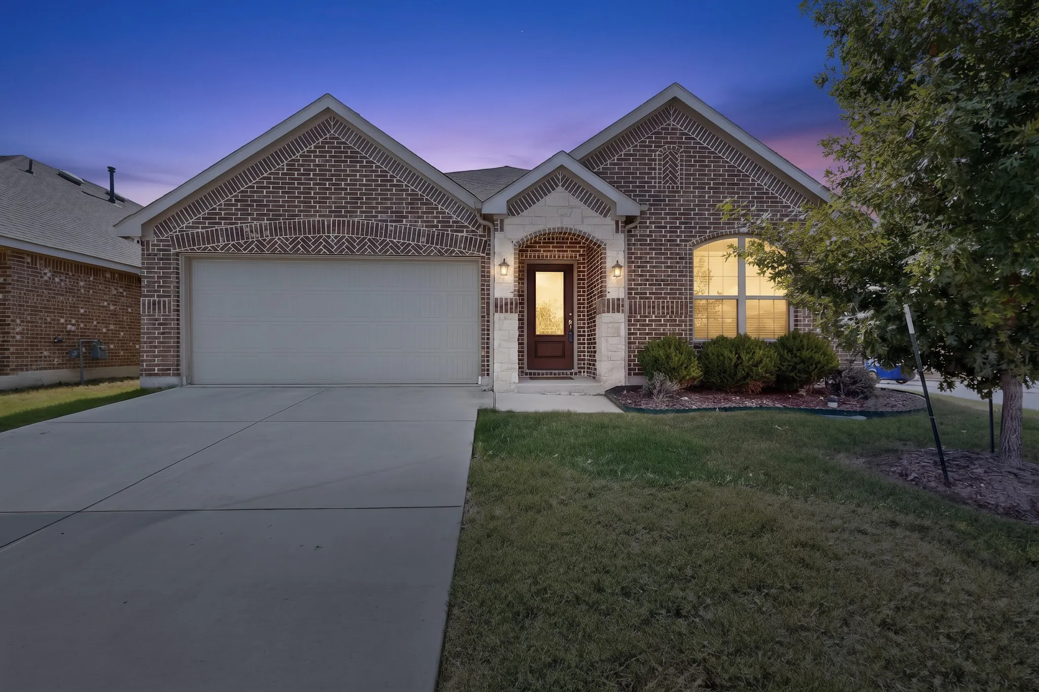 Brick exterior featuring stone accents, arched entryway, concrete driveway, and multi-gabled roofline