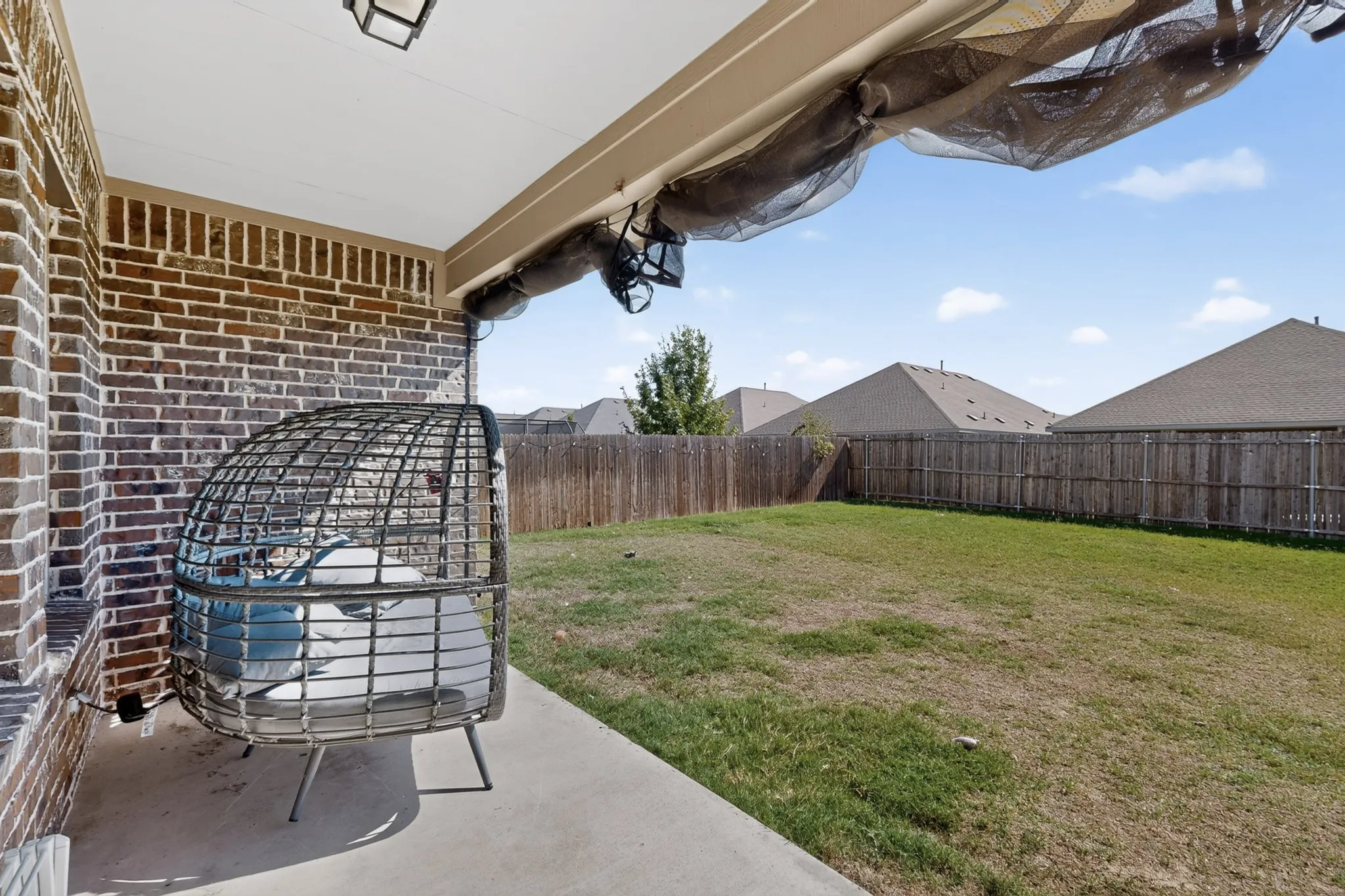 Covered concrete patio with brick exterior wall and wood-style privacy fencing enclosing the backyard