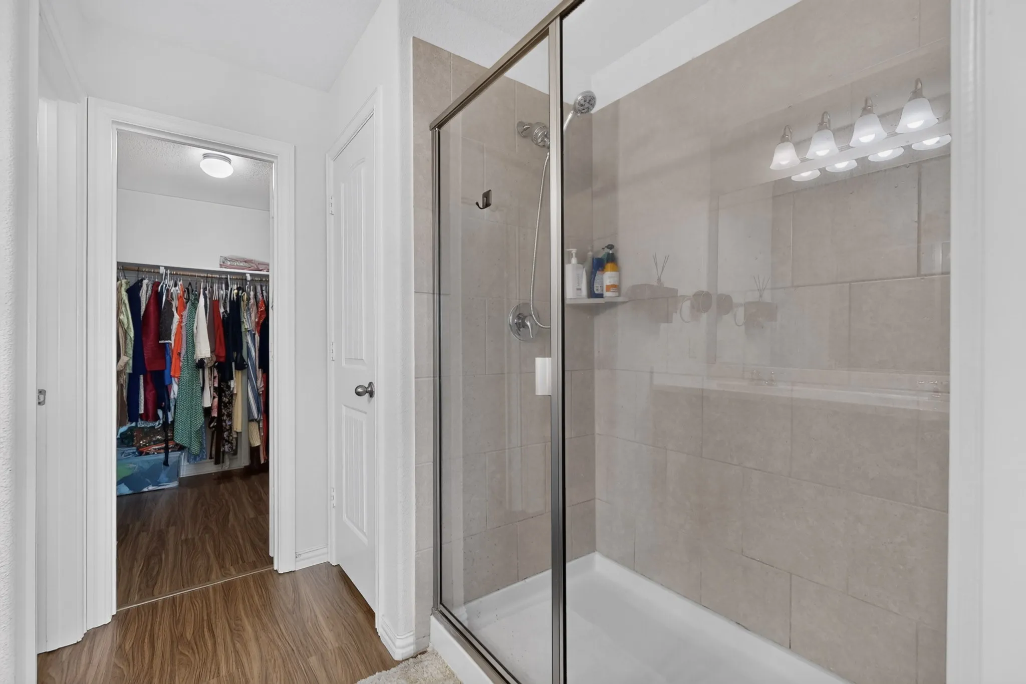 Walk-in shower featuring large-format stone-finish tile surround, chrome fixtures, and a glass enclosure, complemented by wood-finish flooring