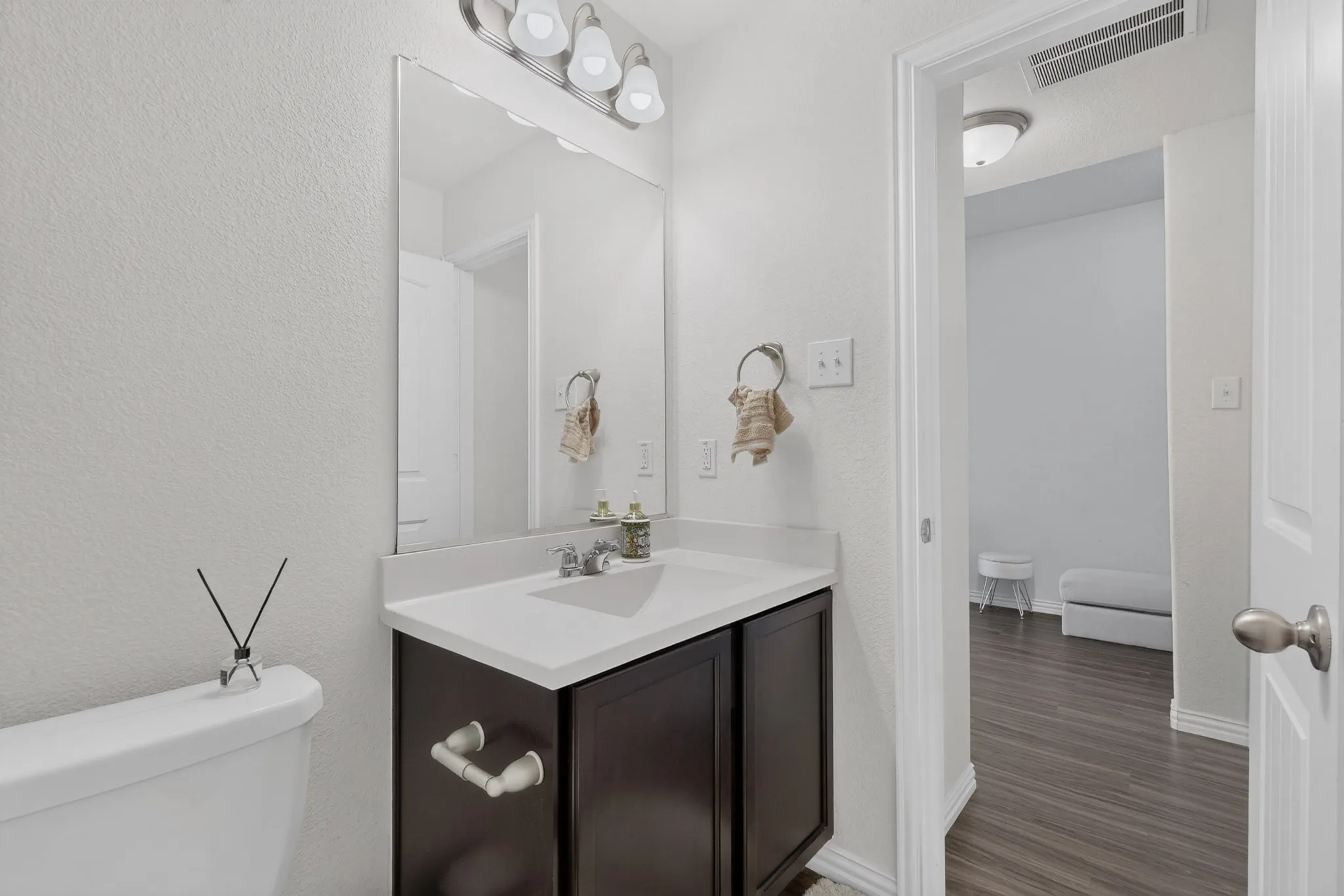 Bathroom featuring a dark-finish vanity cabinet with a white countertop and integrated sink, a full-length wall mirror, and a multi-bulb light fixture