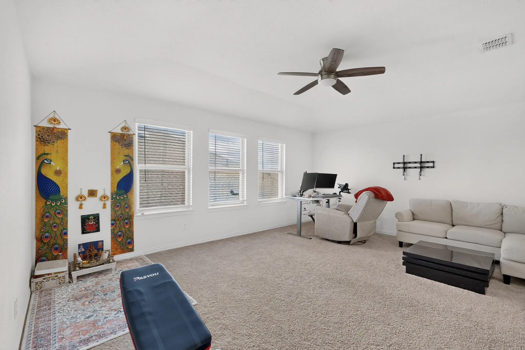 Spacious interior room featuring neutral carpeting, a high ceiling with a ceiling fan, and three windows