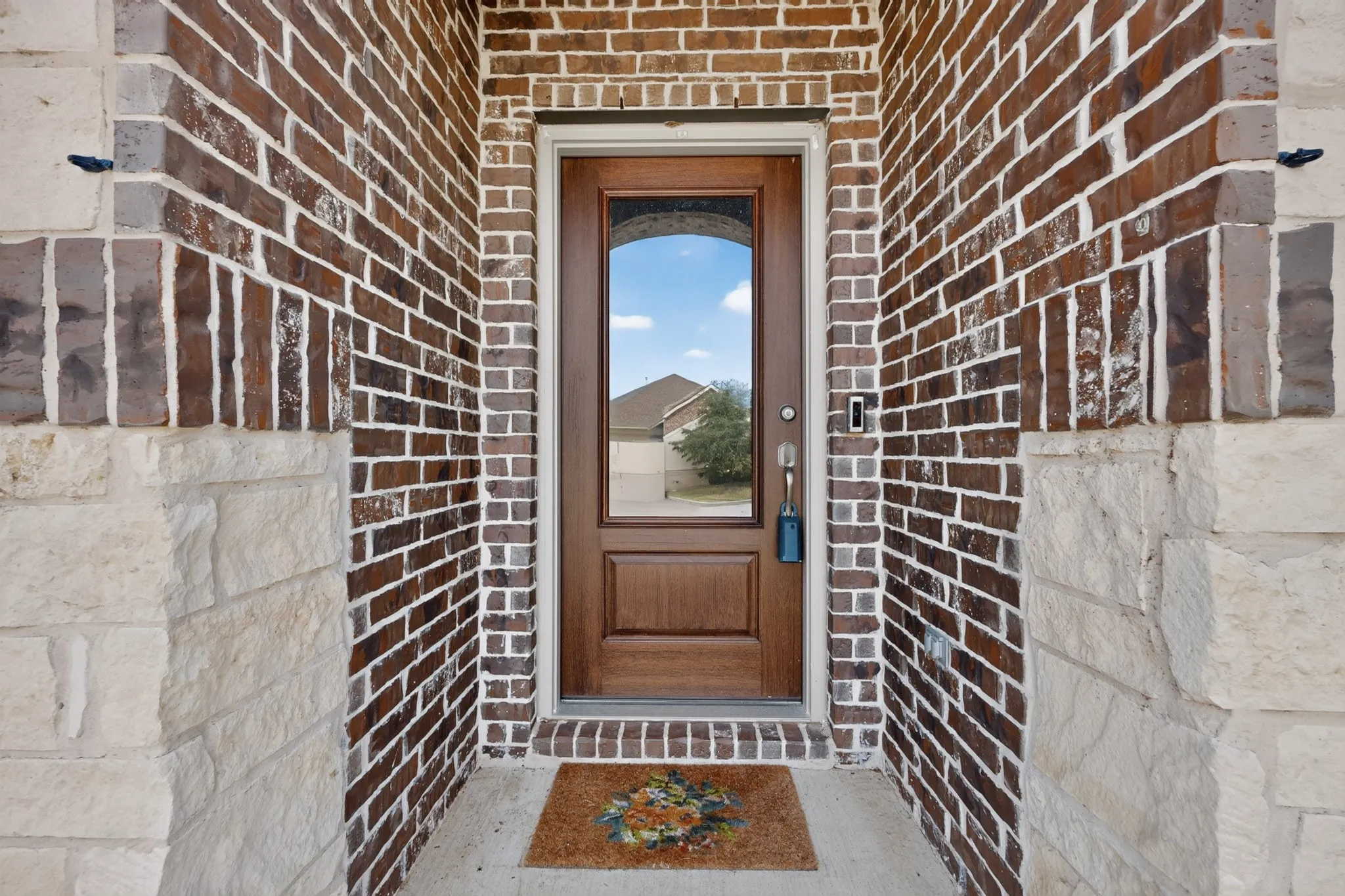 Entryway featuring a wood-finish door with a central glass panel, encased in a multi-textured facade of red brick and natural stone masonry