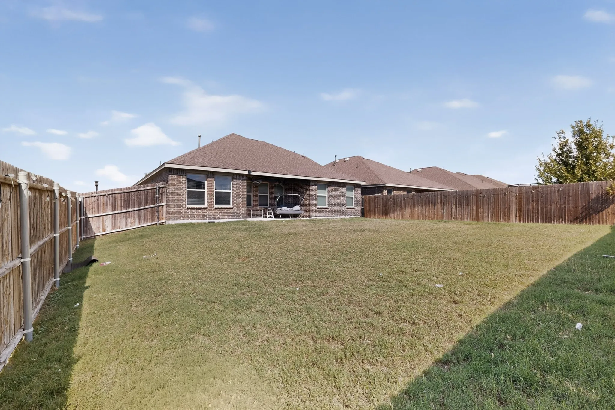 Spacious backyard featuring a brick exterior, shingle roof, and wooden privacy fencing