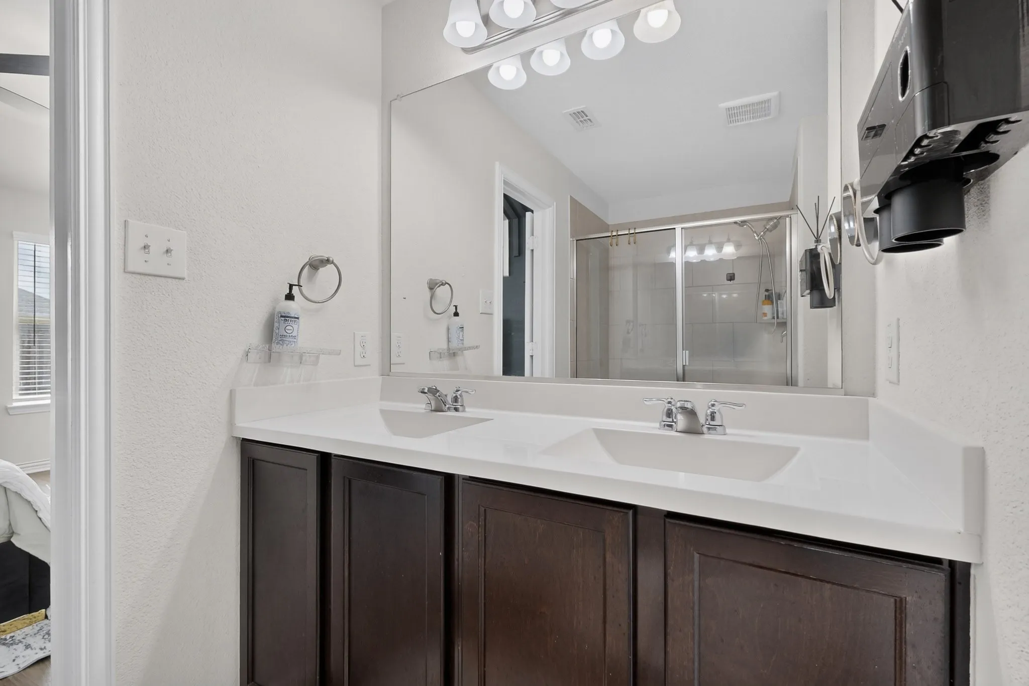 Dual-sink vanity with dark wood-finish cabinetry, solid-surface countertop, full-width mirror, and polished chrome fixtures