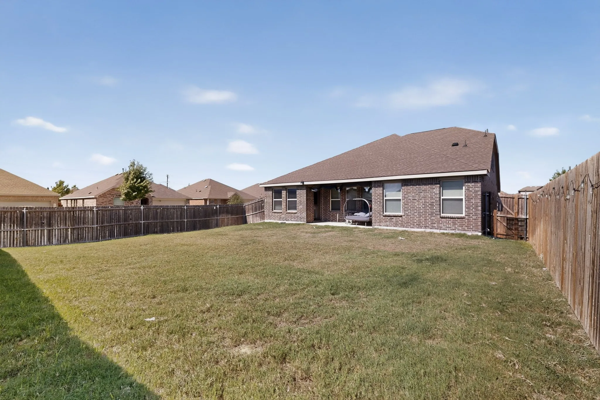 Brick exterior with a gabled roofline, covered patio, and wood privacy fencing enclosing the backyard