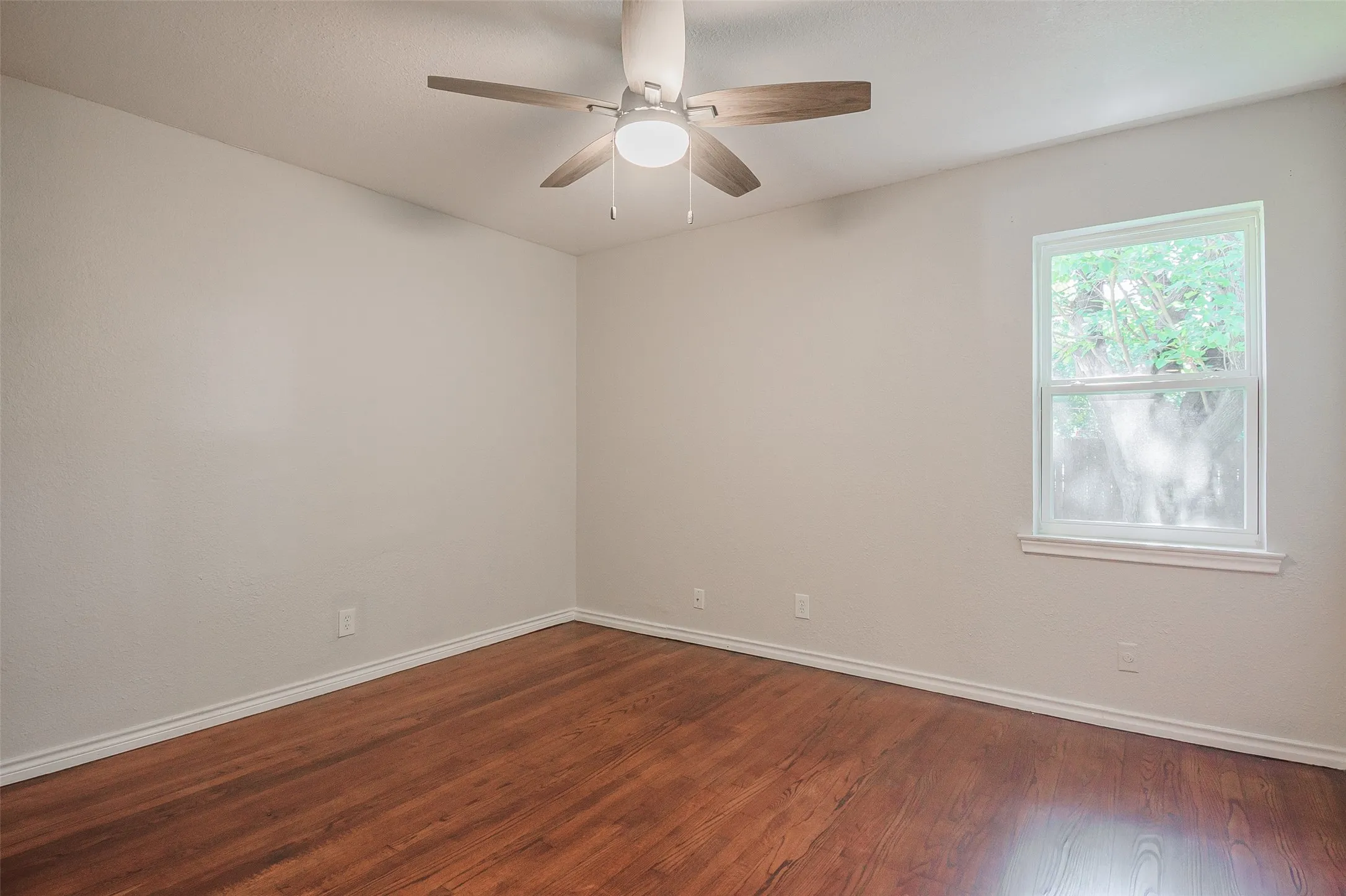 Room featuring wood-finish flooring, a neutral wall color palette, a ceiling fan with integrated lighting, and a single-pane window