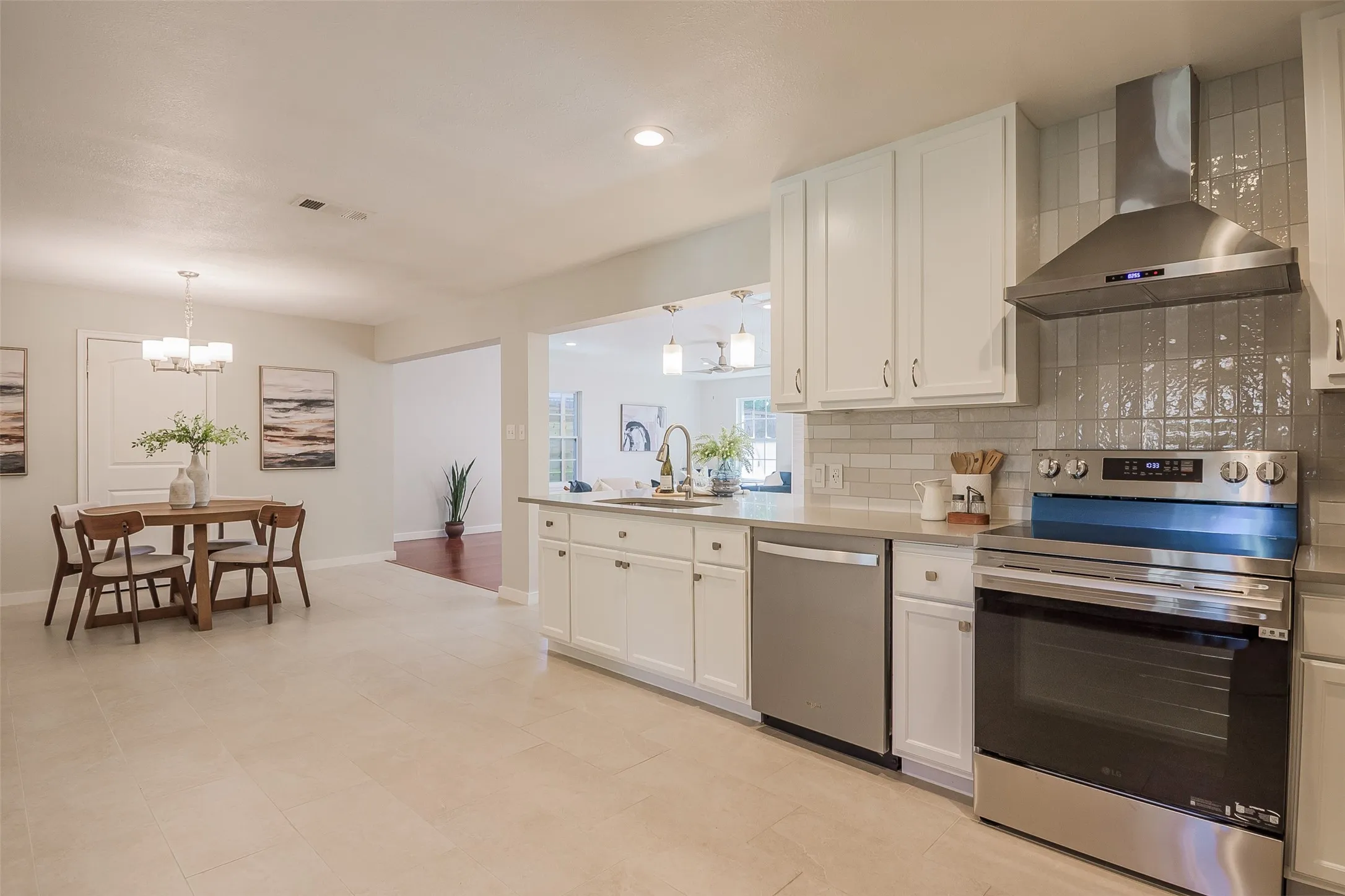 Kitchen featuring white cabinetry, solid-surface countertops, subway tile backsplash, stainless steel appliances, and a range hood