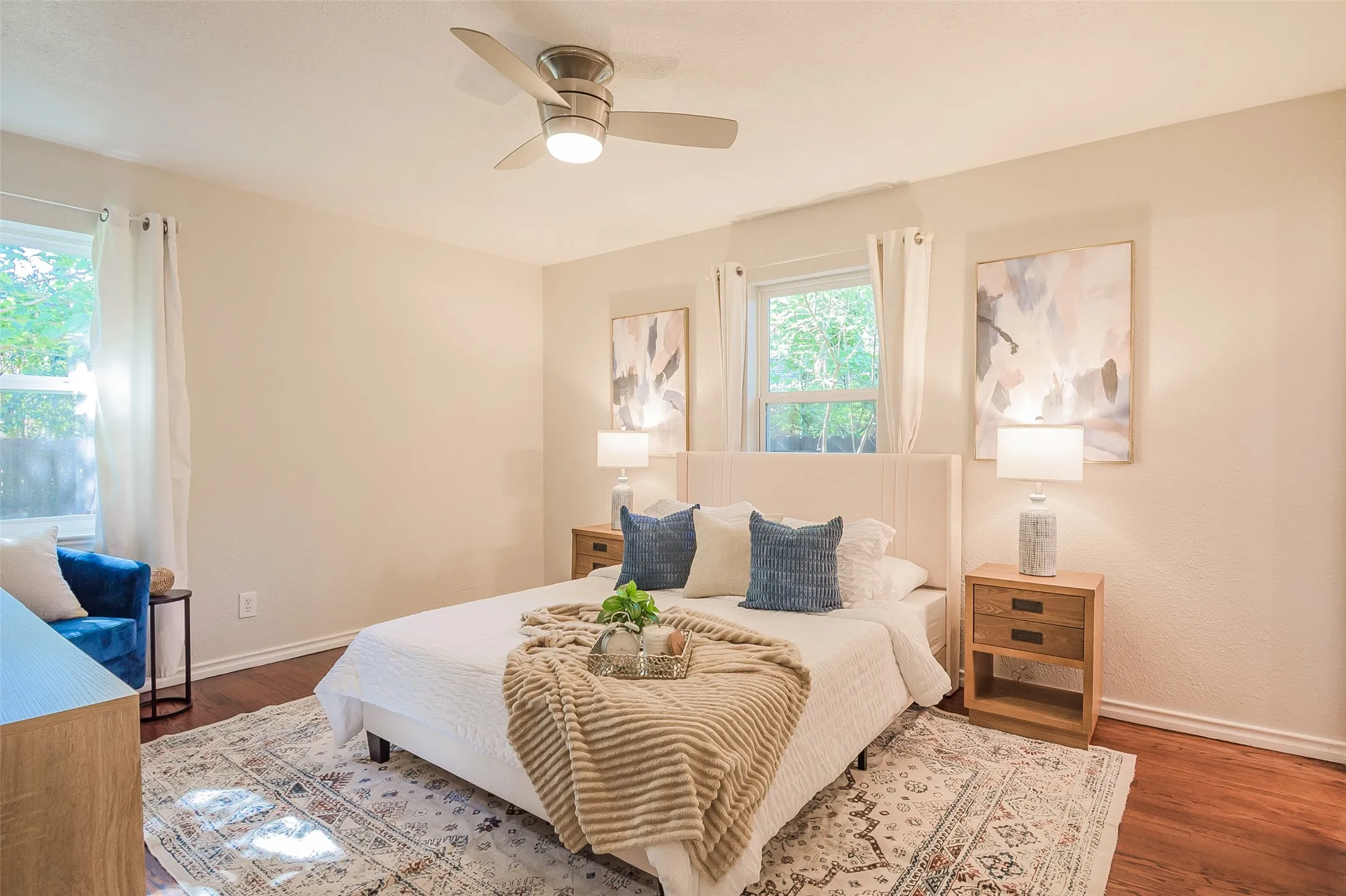 Room featuring wood-finish flooring, neutral wall paint, two dual-pane windows, and a brushed nickel ceiling fan with integrated lighting
